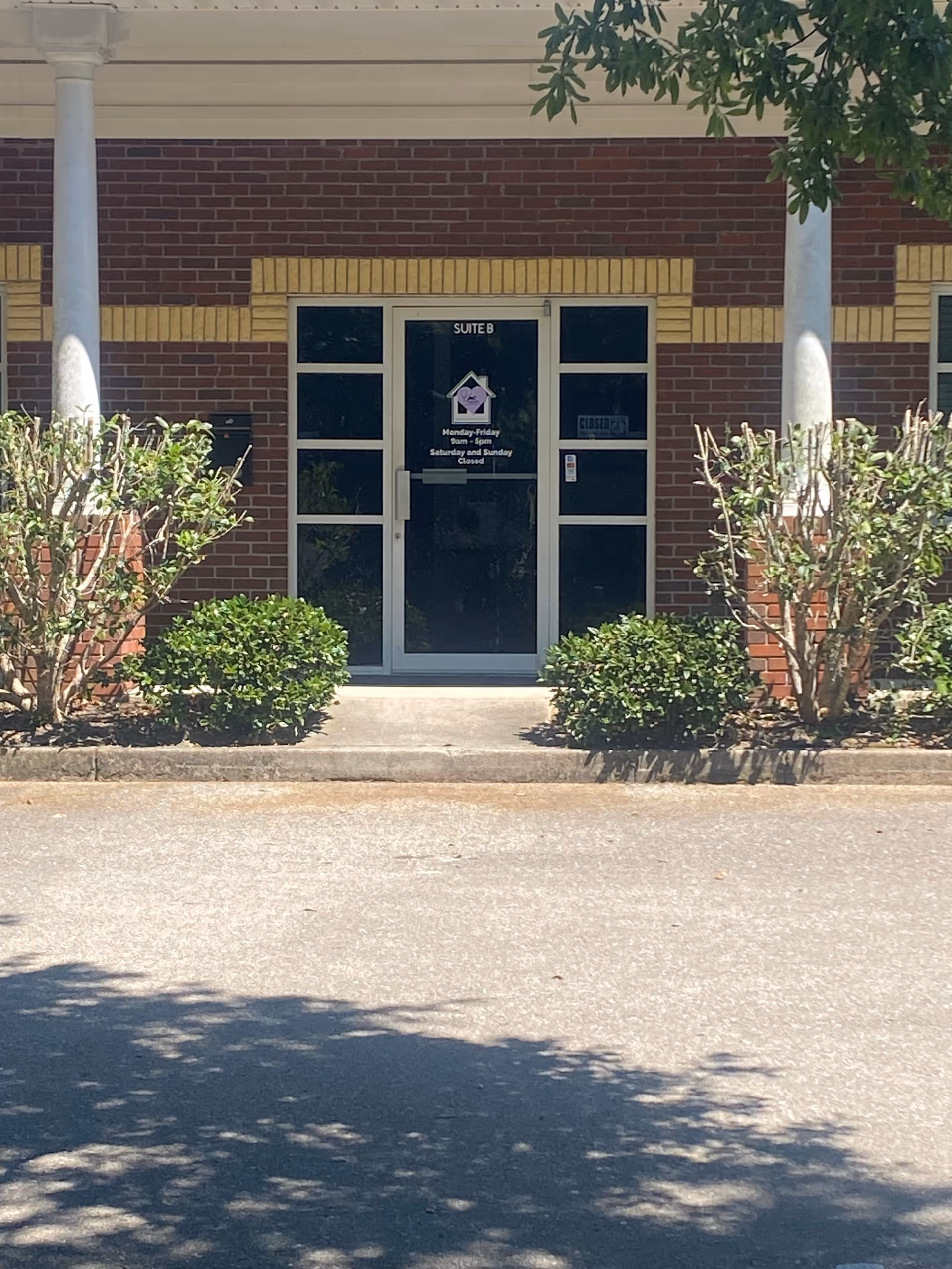 Brick exterior of senior facility with glass entrance door labeled Suite B, surrounded by shrubs.
