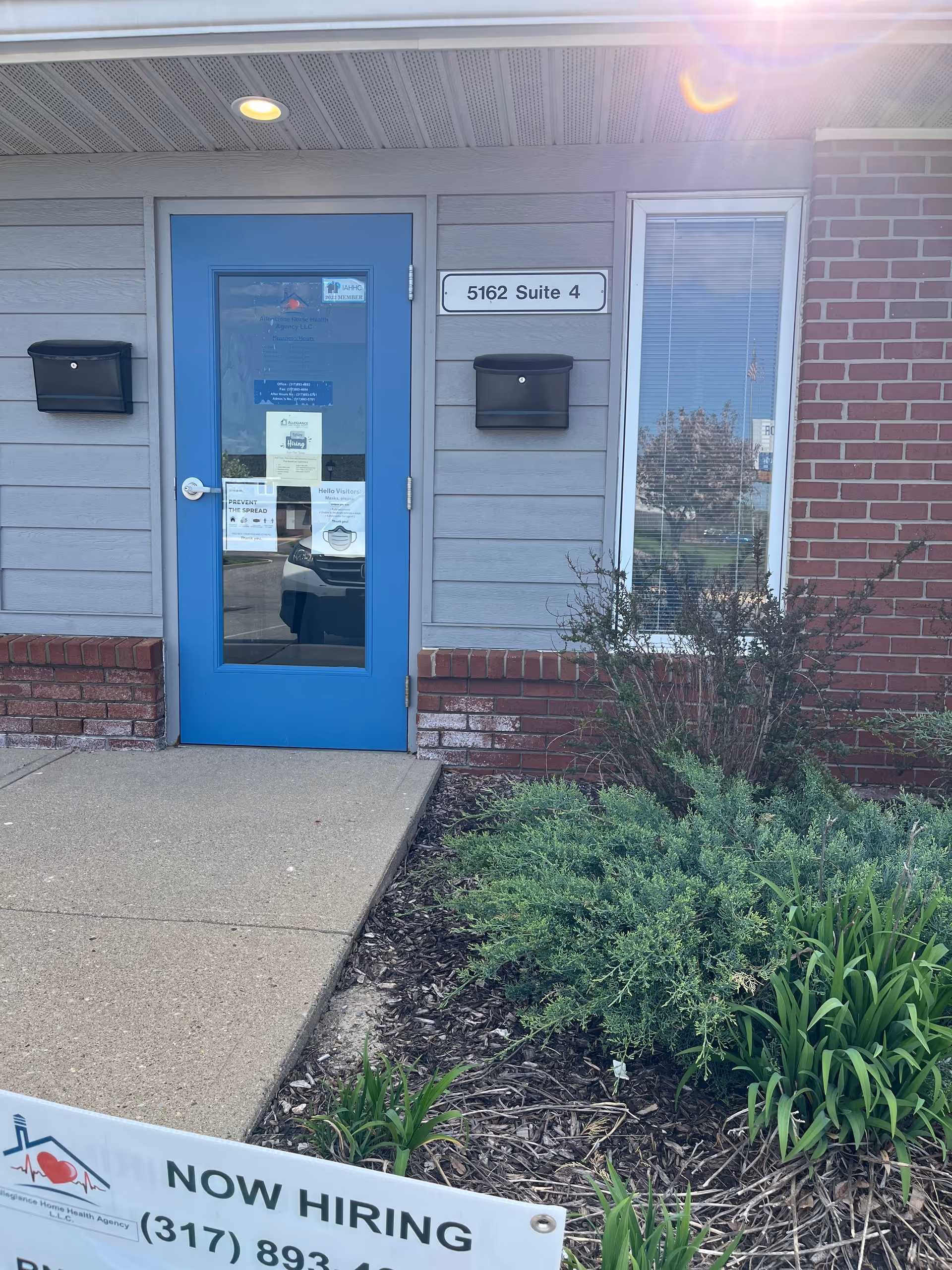 Blue exterior door with glass panel, mailboxes, window, and Now Hiring sign outside.