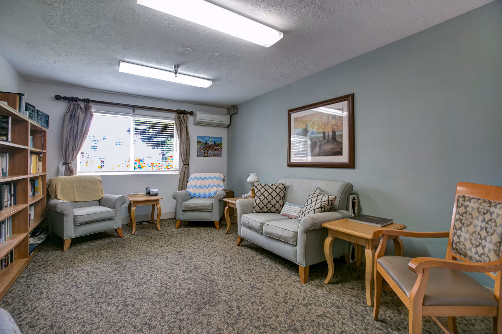 Common living room with couches, chairs, bookshelves, and a window.