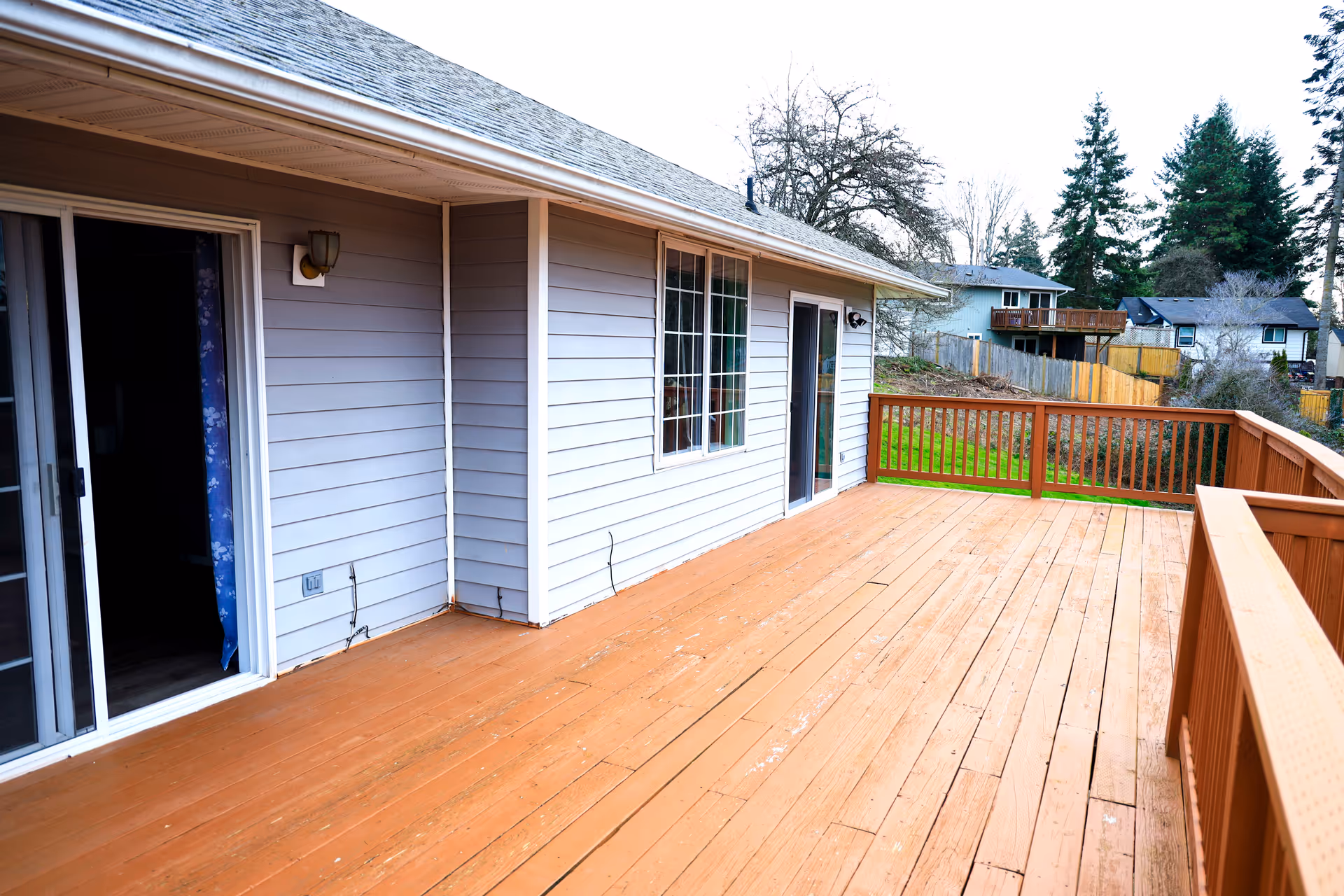Backyard wooden deck attached to a light gray house with sliding doors.