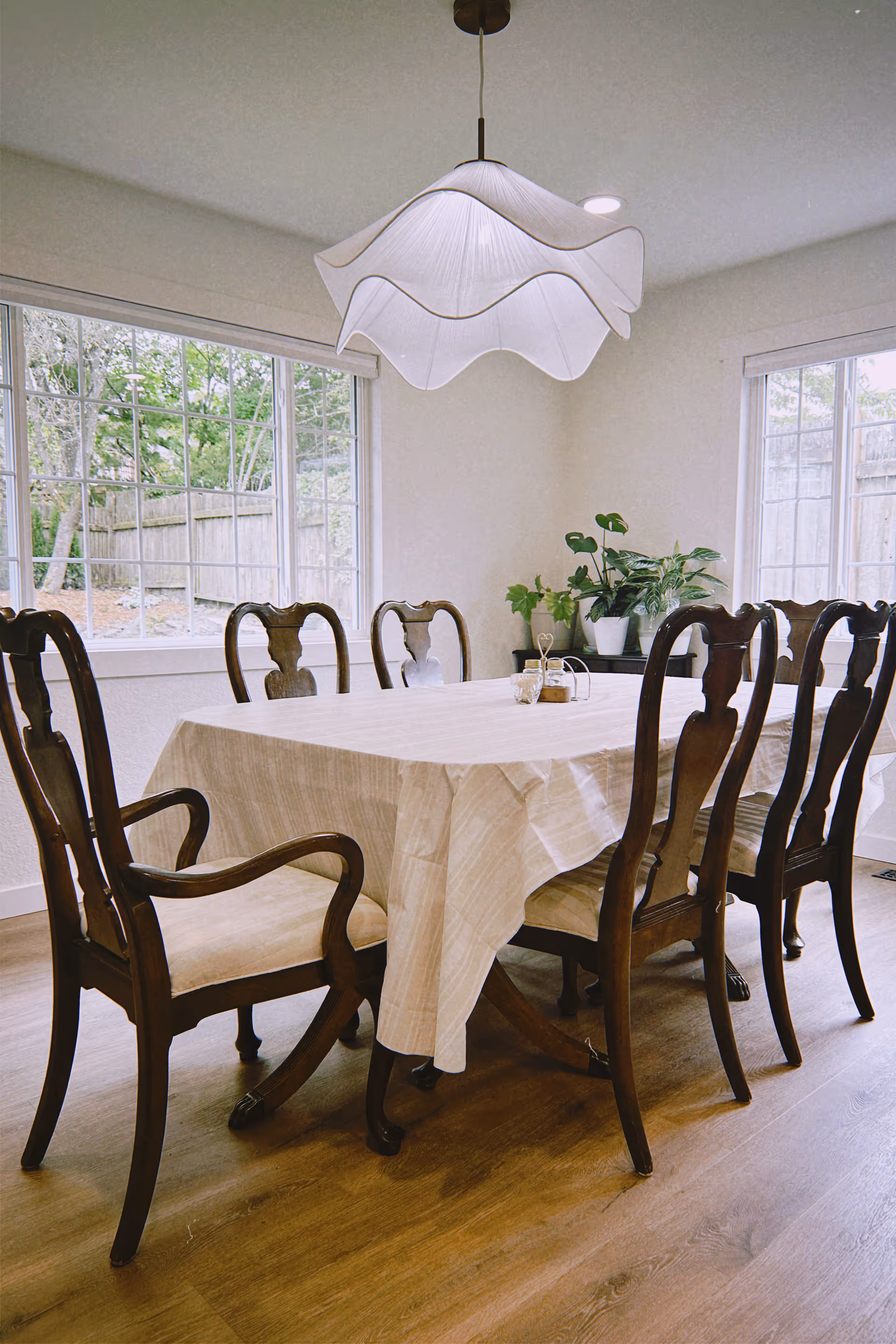 A dining room with a large table, wooden chairs, plants, and a pendant light.