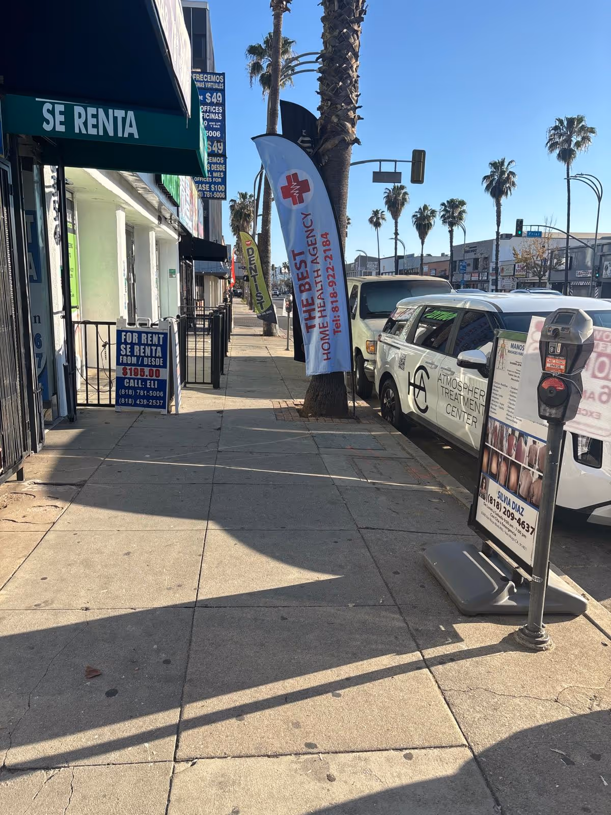 Sidewalk view with storefronts, banners, and a parked van advertising a home health agency.