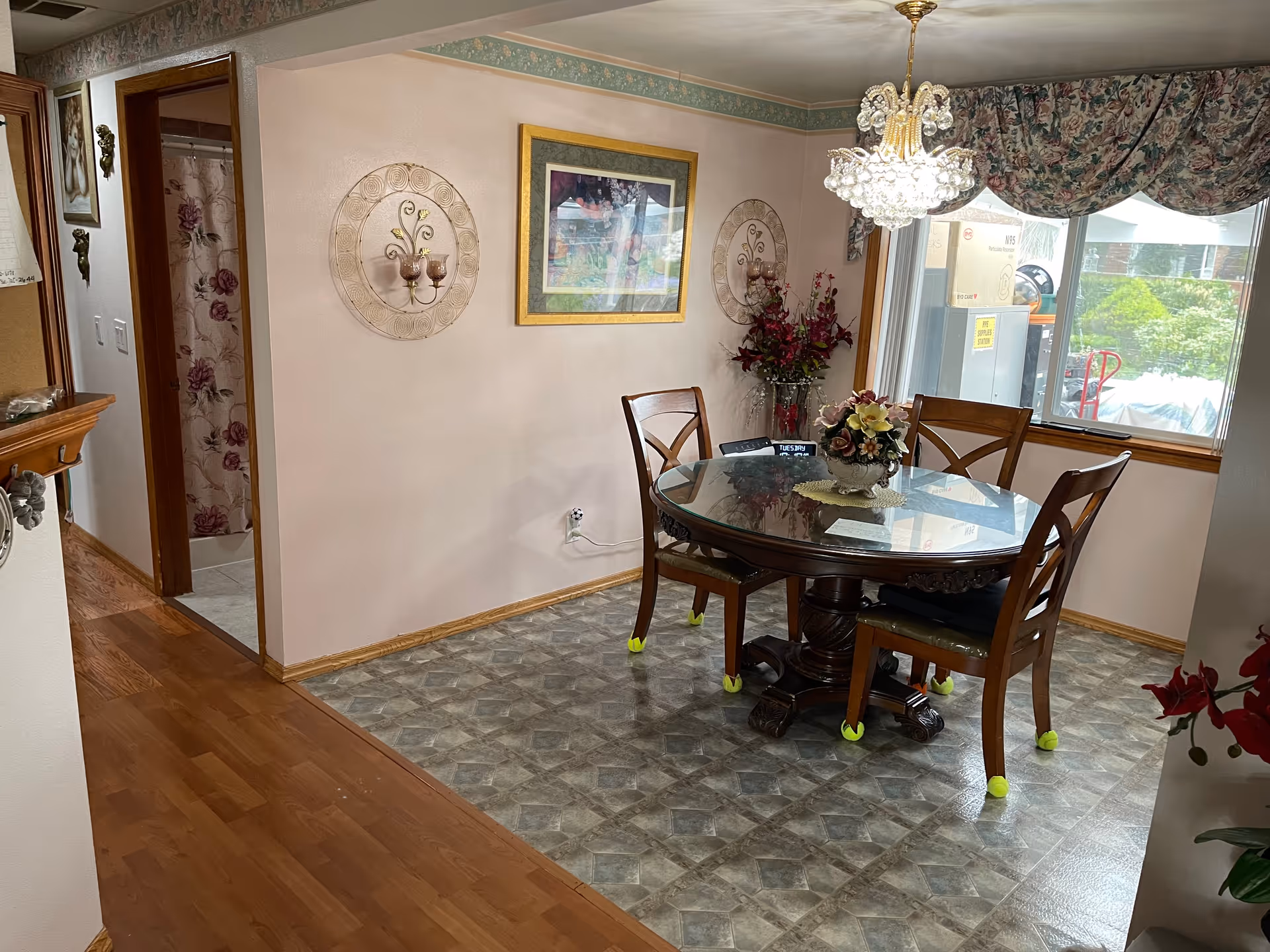 Round glass dining table with four chairs, chandelier, and floral decor in a dining room.