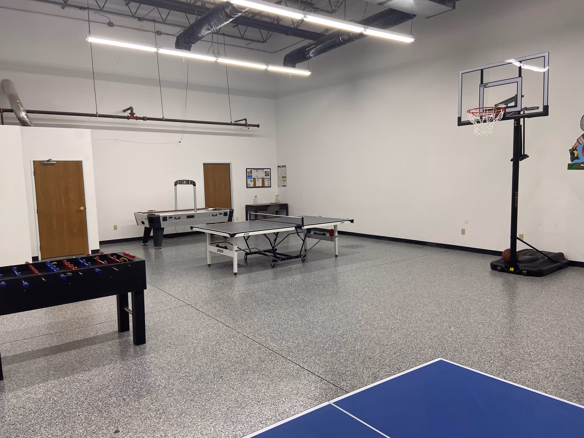 An interior recreation room with pool table, ping pong table, foosball, and basketball hoop.