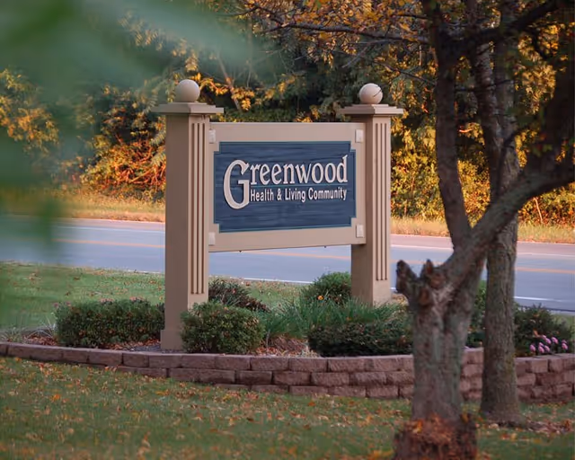 A Greenwood Health & Living Community sign in a landscaped roadside garden.