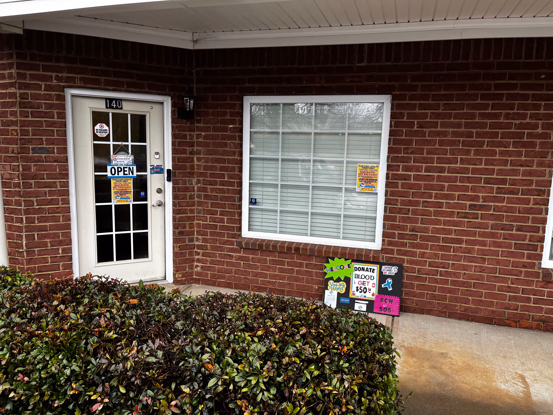 Brick building front with a glass-pane door labeled OPEN and a large window beside.