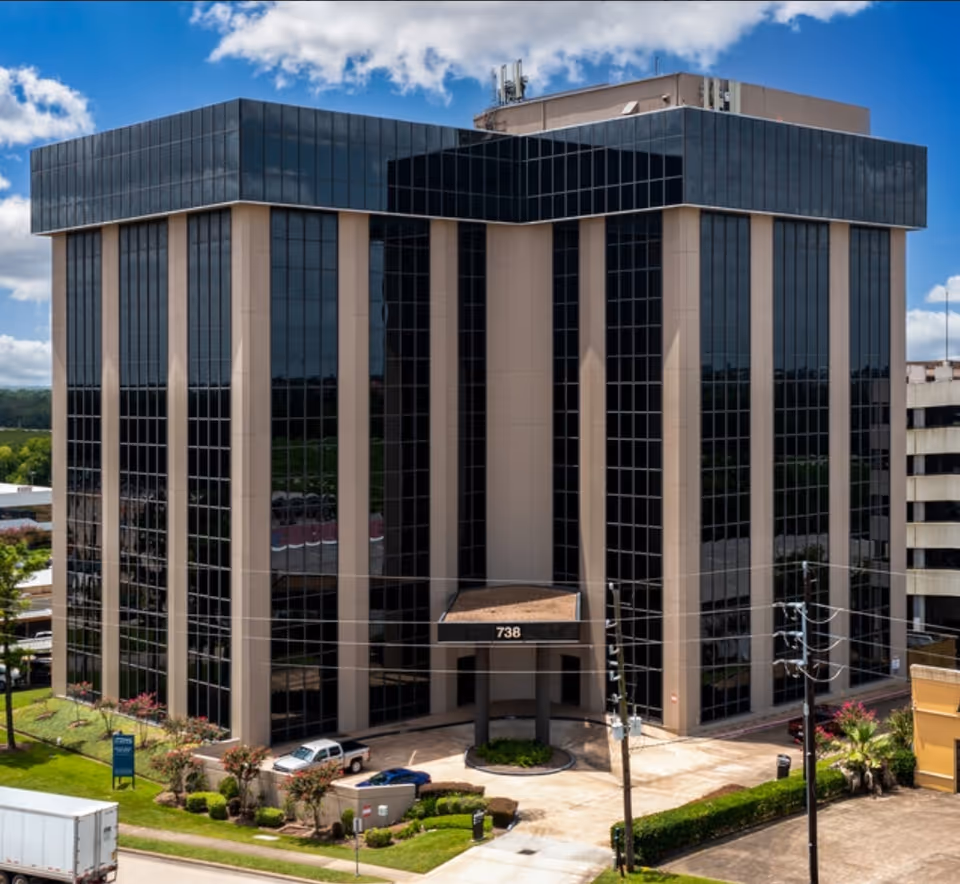 Front view of a tall glass building with beige vertical columns and an entrance canopy.