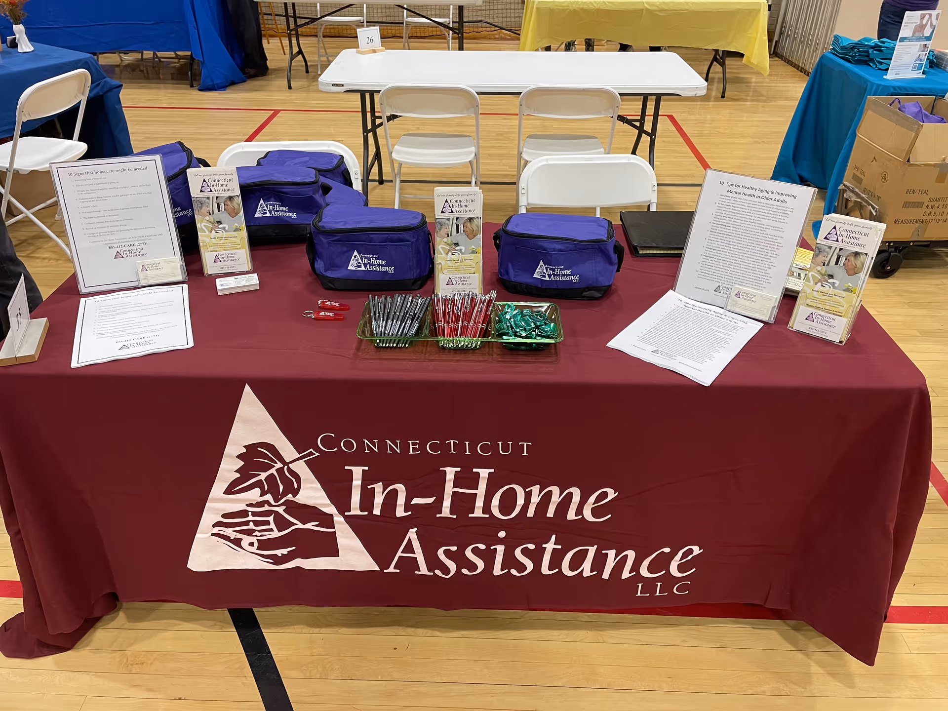 Indoor event booth with a maroon tablecloth and Connecticut In-Home Assistance promotional materials.