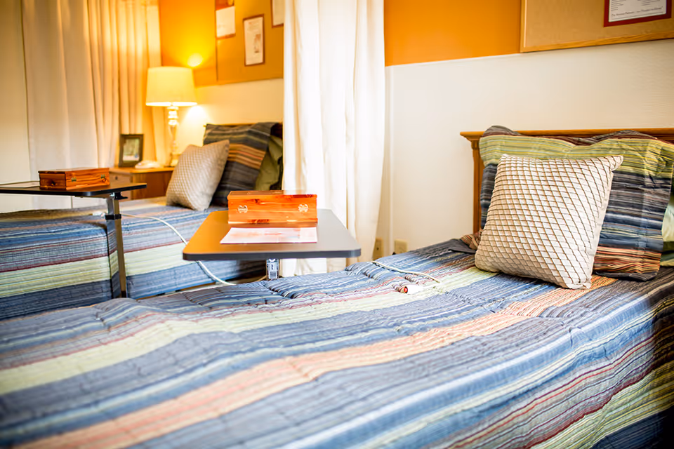 Two striped beds in a warm senior living bedroom with pillows, lamp, and side table.