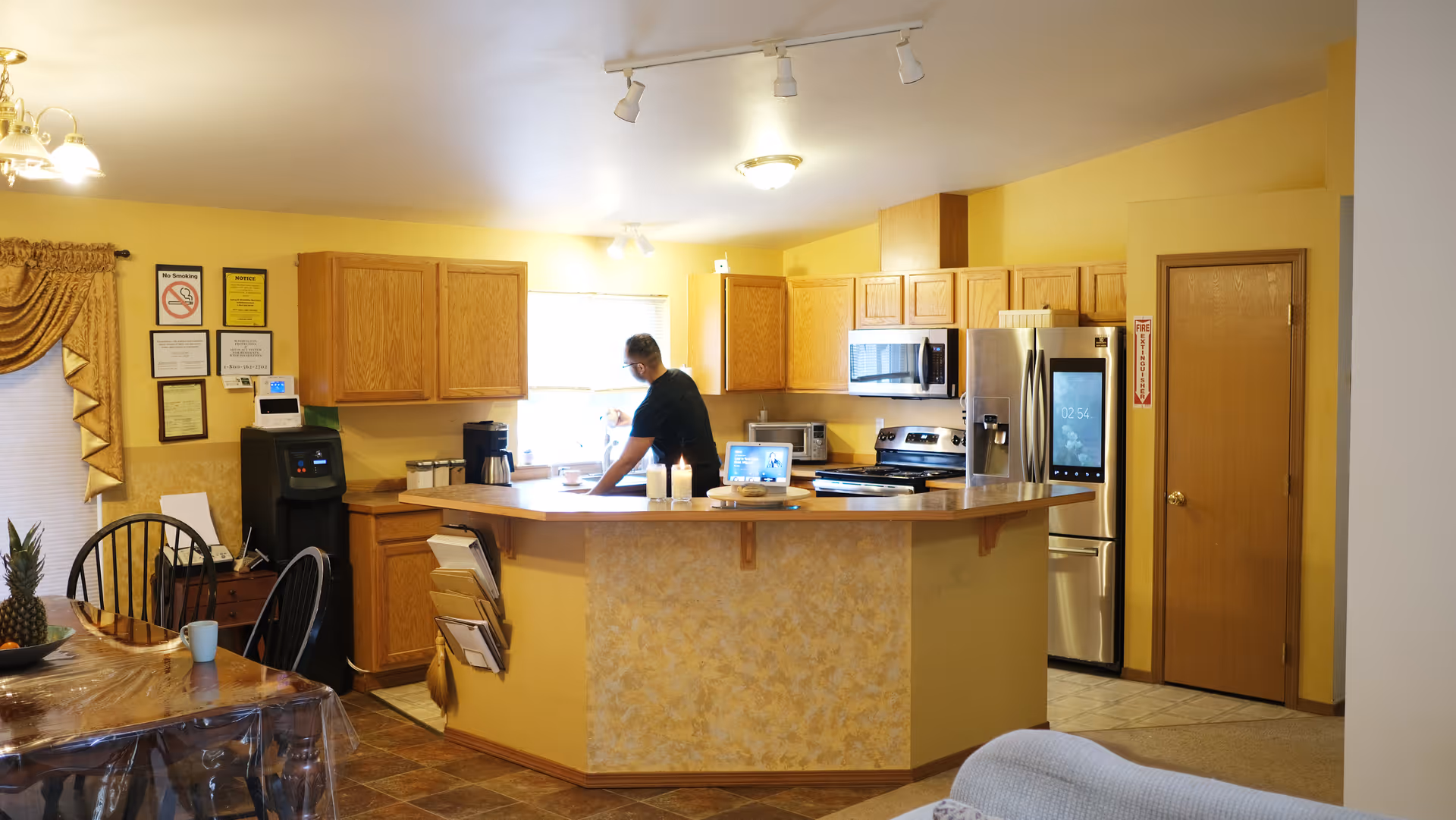 Bright kitchen in a senior living facility with cabinets and a person at the counter.