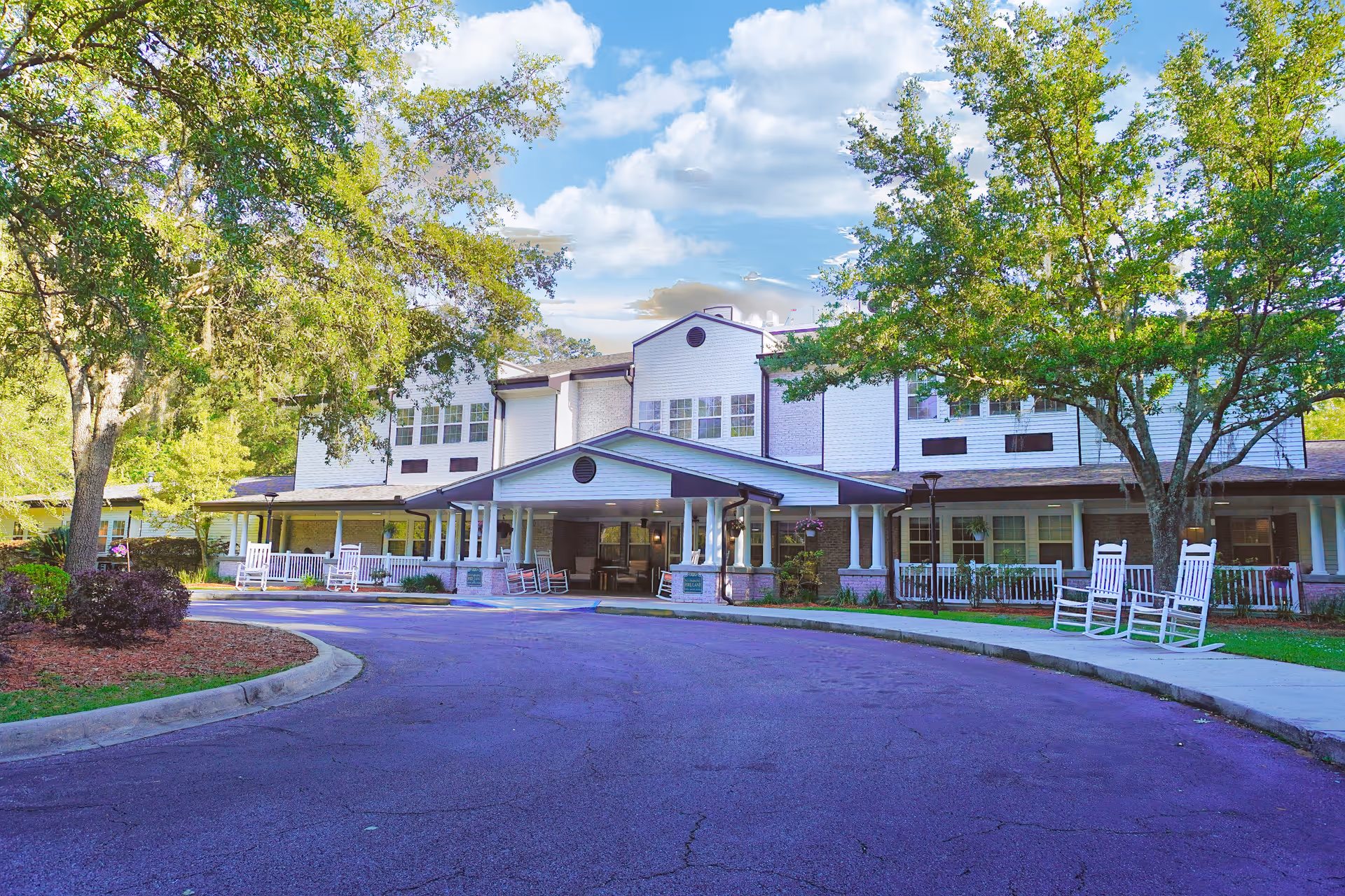 Exterior view of Sodalis Tallahassee Assisted Living with a curved driveway and rocking chairs.