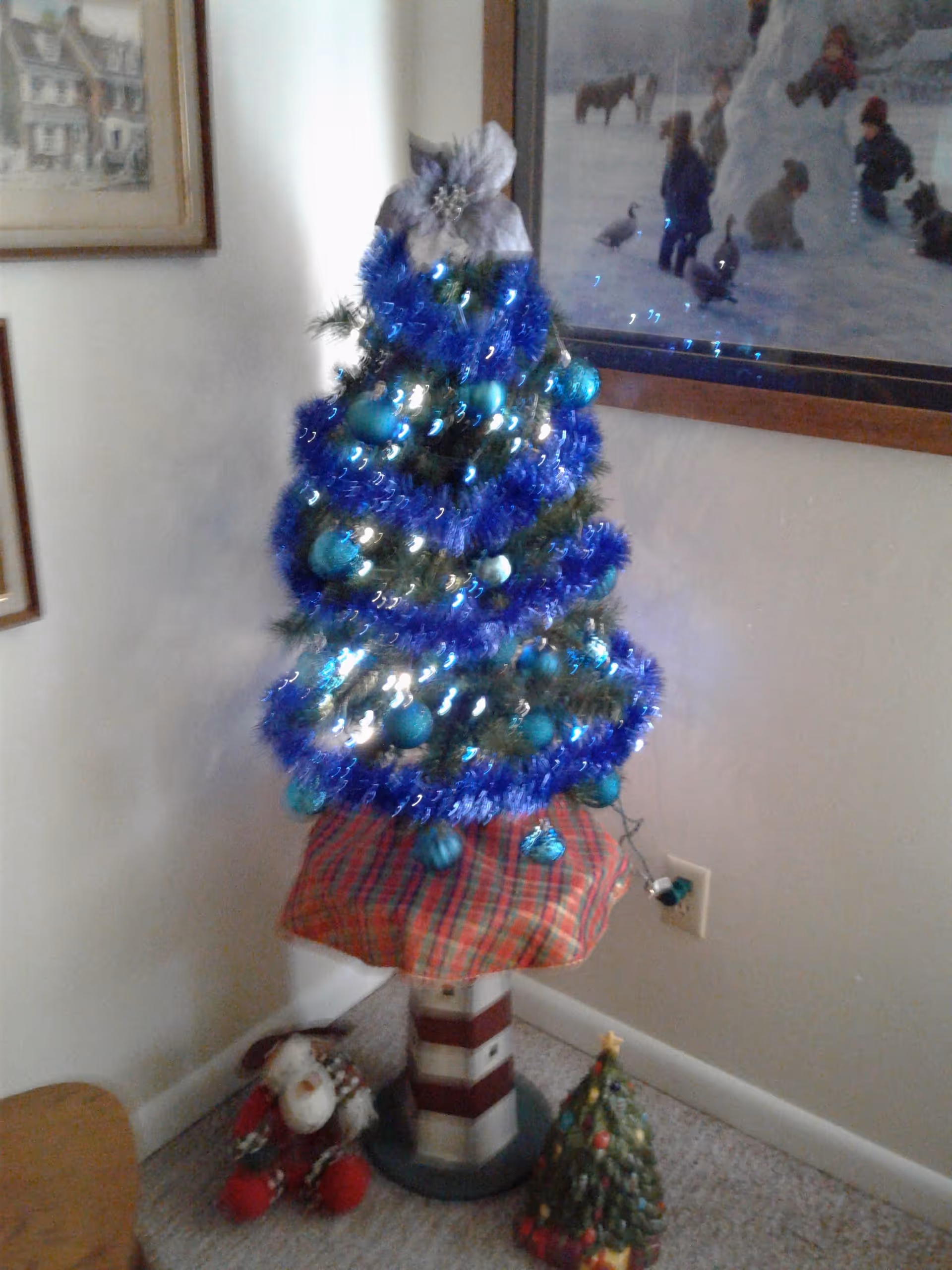 Blue tinsel Christmas tree with ornaments stands in a decorated corner of a cozy interior.