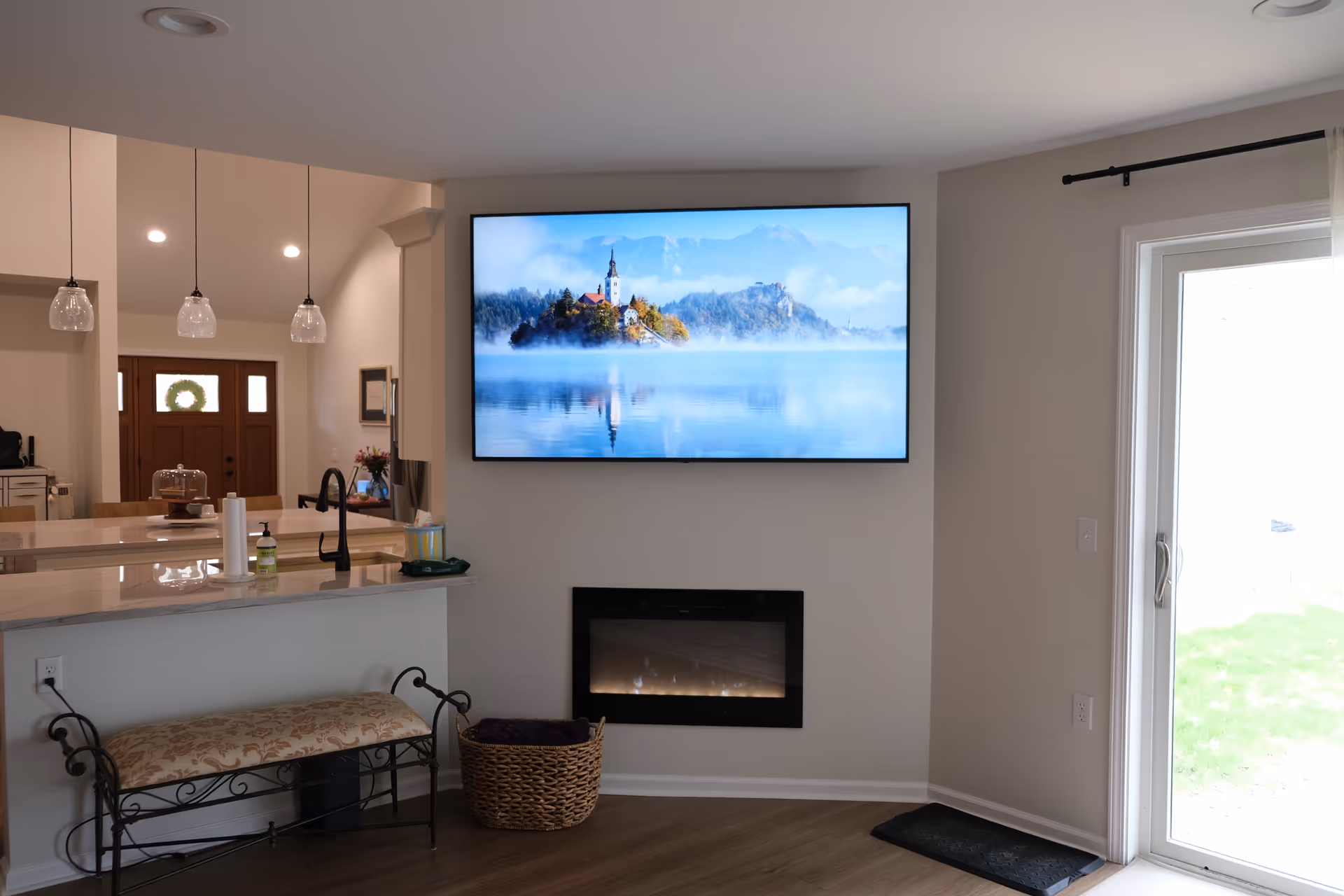 Open-concept living area with kitchen counter, wall TV, fireplace, bench, and glass door.
