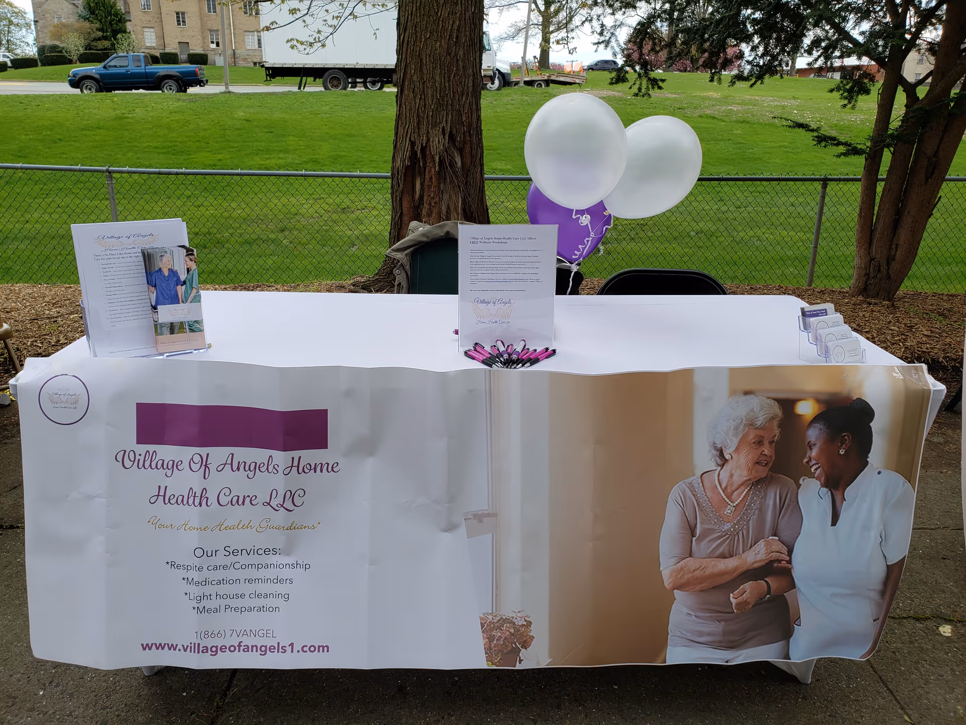 Outdoor health care booth with banner, table, and balloons for Village Of Angels Home Health Care.
