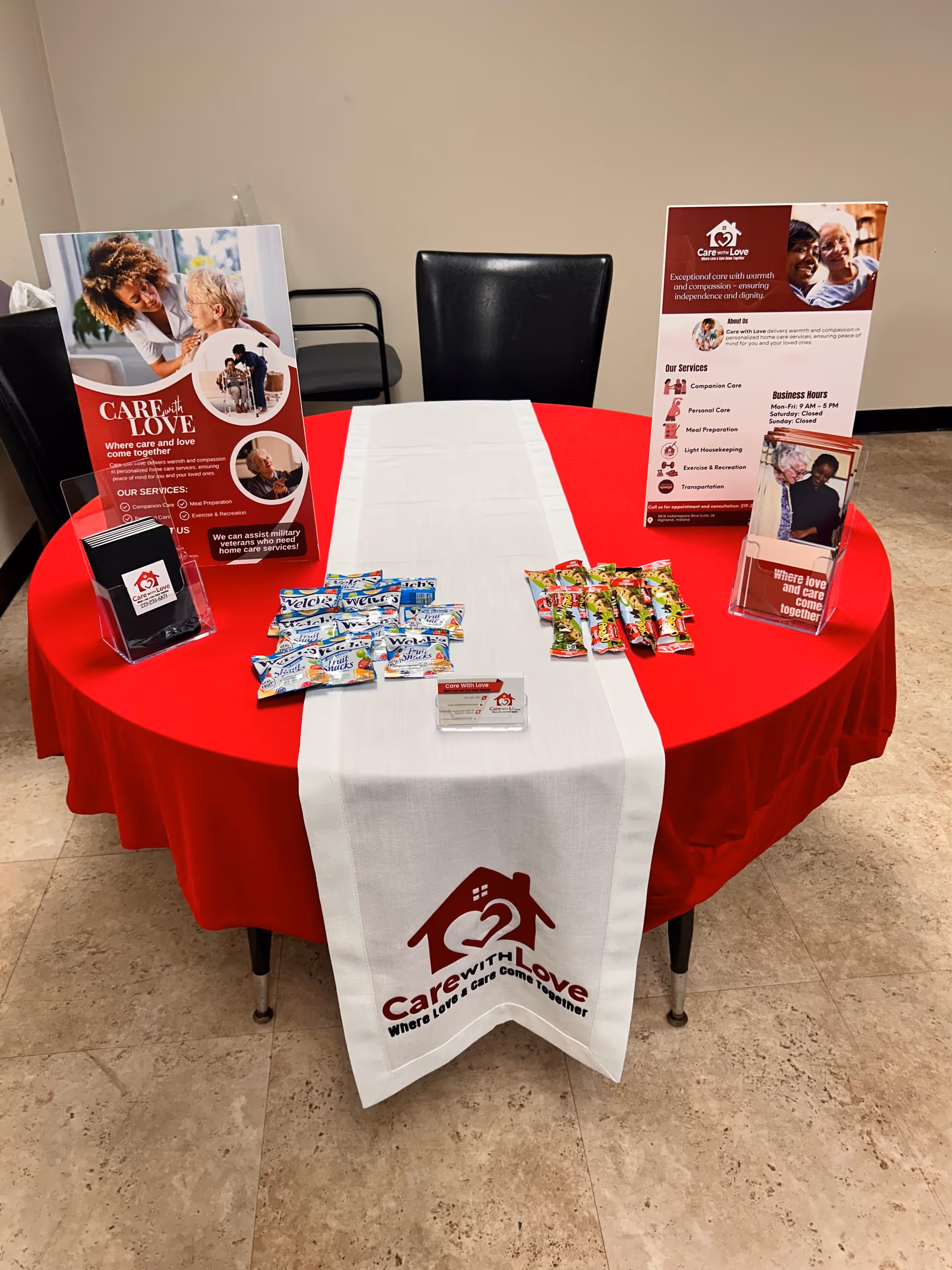Round red table with white runner displaying Care With Love brochures inside a hallway.