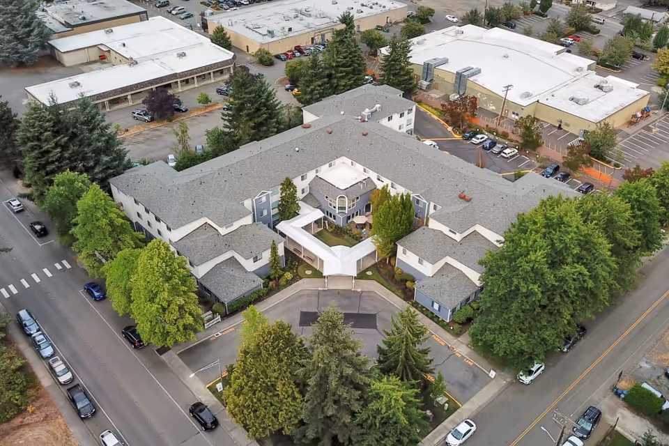 Aerial view of Mountlake Terrace Plaza showing a U-shaped multi-story senior living building with a covered entrance, surrounding trees and parking areas.