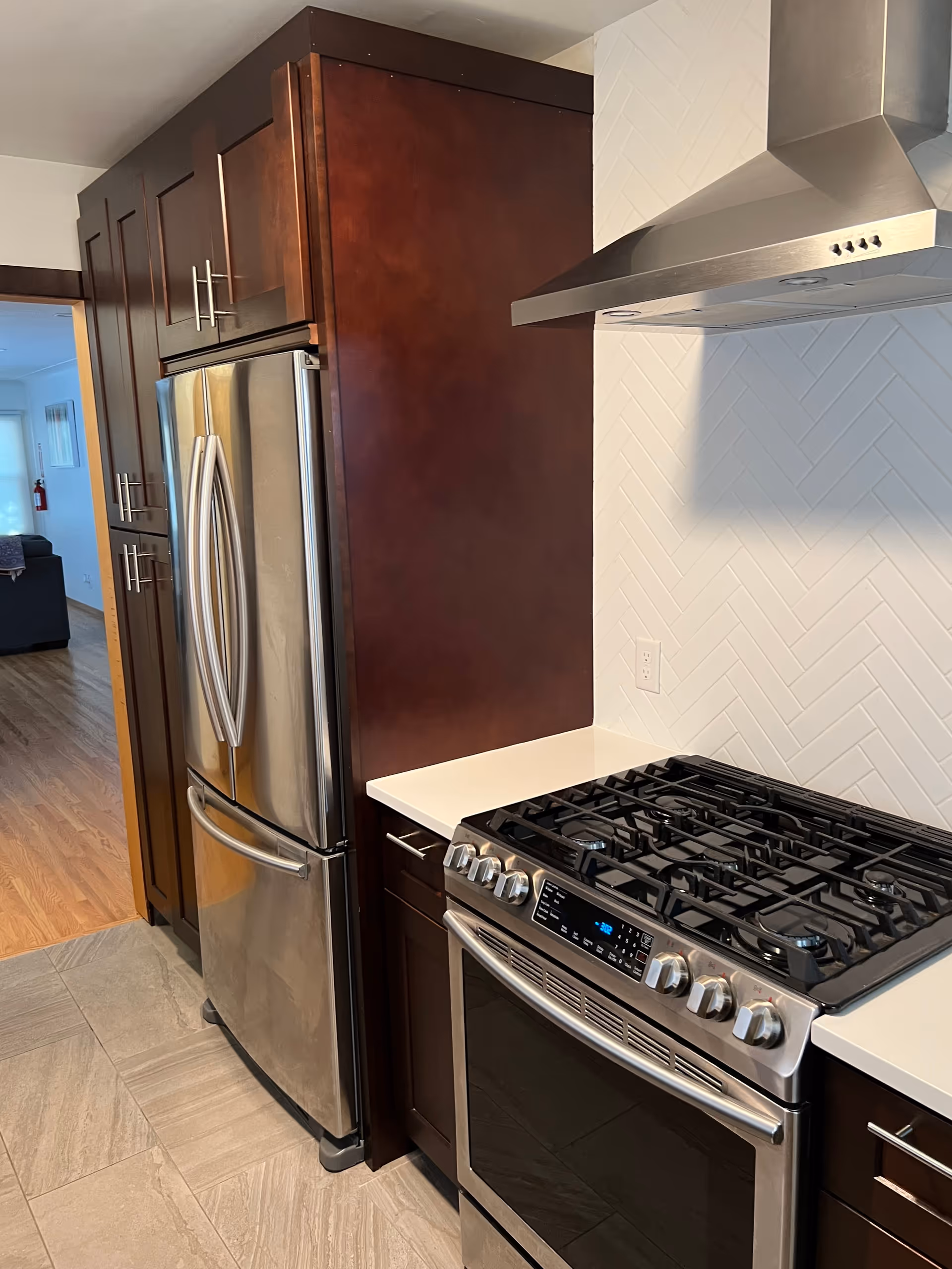 A modern kitchen with stainless steel refrigerator, gas range, dark wood cabinets, and white tile backsplash