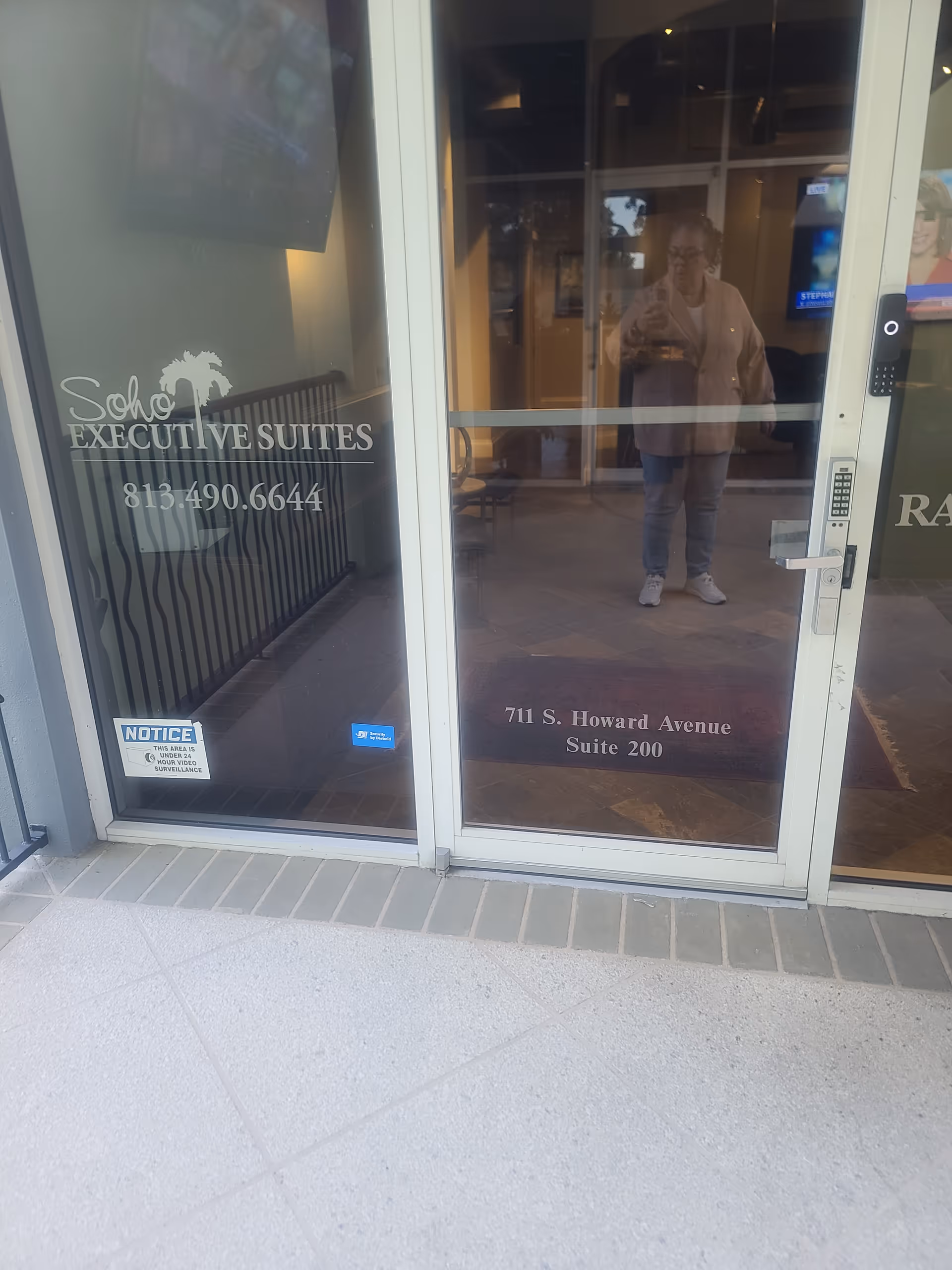 Glass entry door reflects a person; signage shows Soho Executive Suites and address.