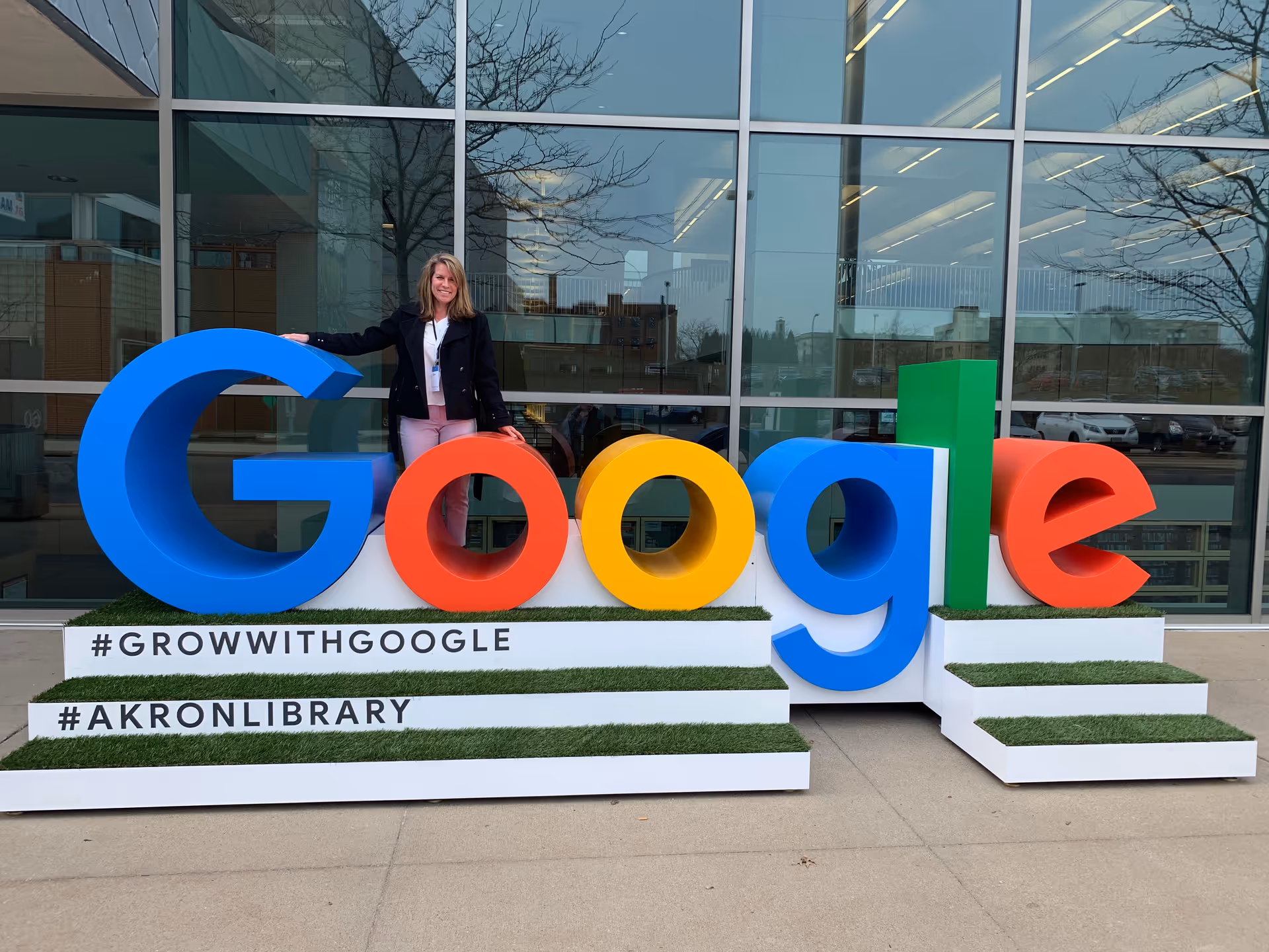 A woman stands beside oversized Google letters outside a glass-front building.