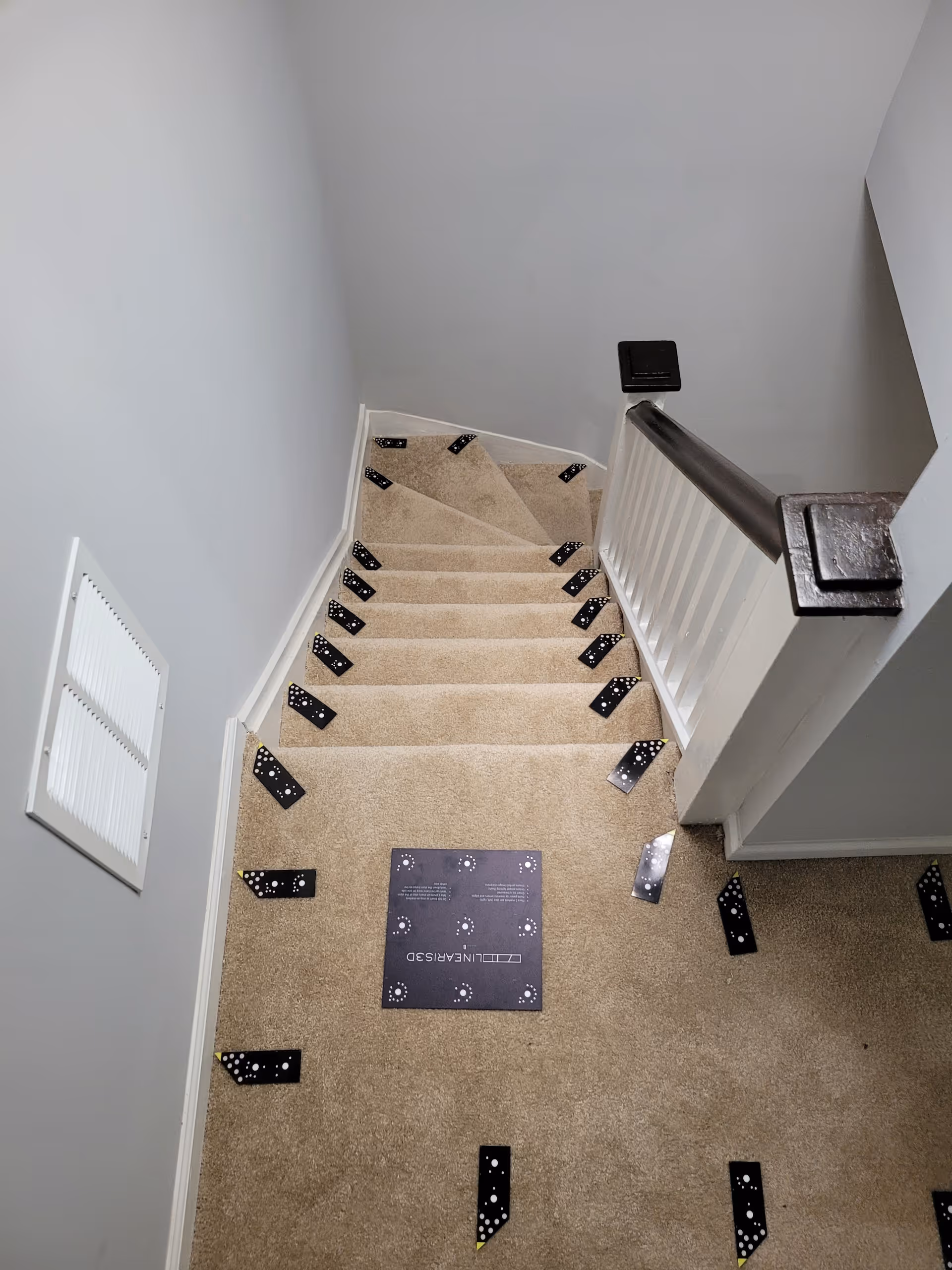An indoor stairwell with beige carpet, white walls, and scattered domino-shaped black tiles.