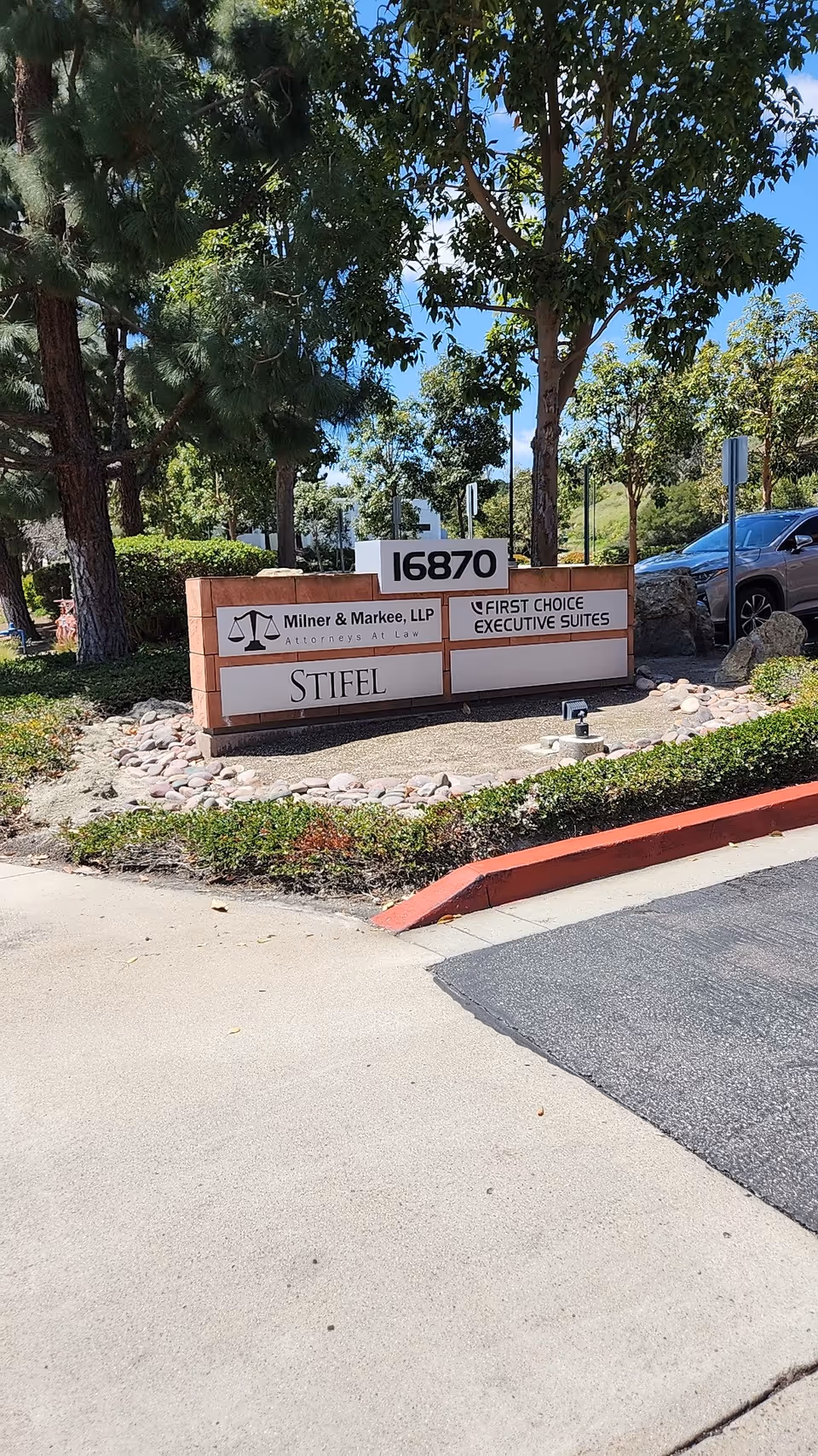Exterior view of a small landscaped area with a sign displaying 16870 and multiple business names.