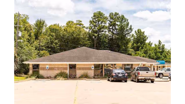 Exterior view of a single-story clinic with parking lot and trees in the background.