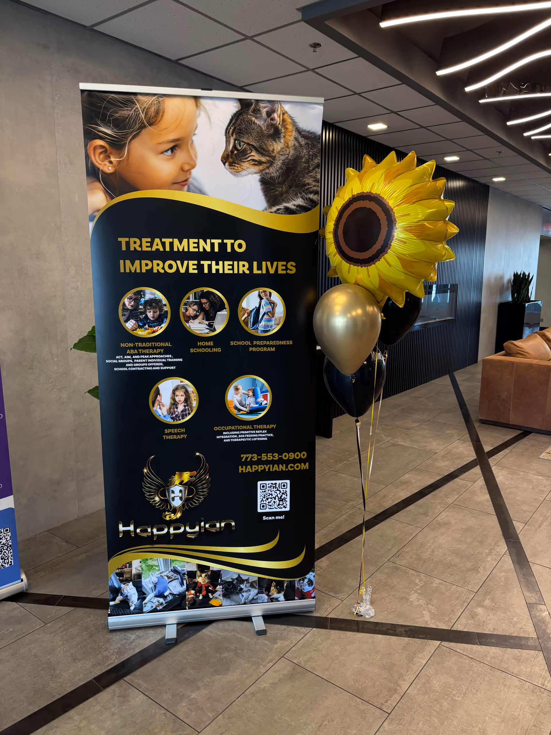 Roll-up banner advertising Happyian services beside sunflower balloons in a modern lobby.
