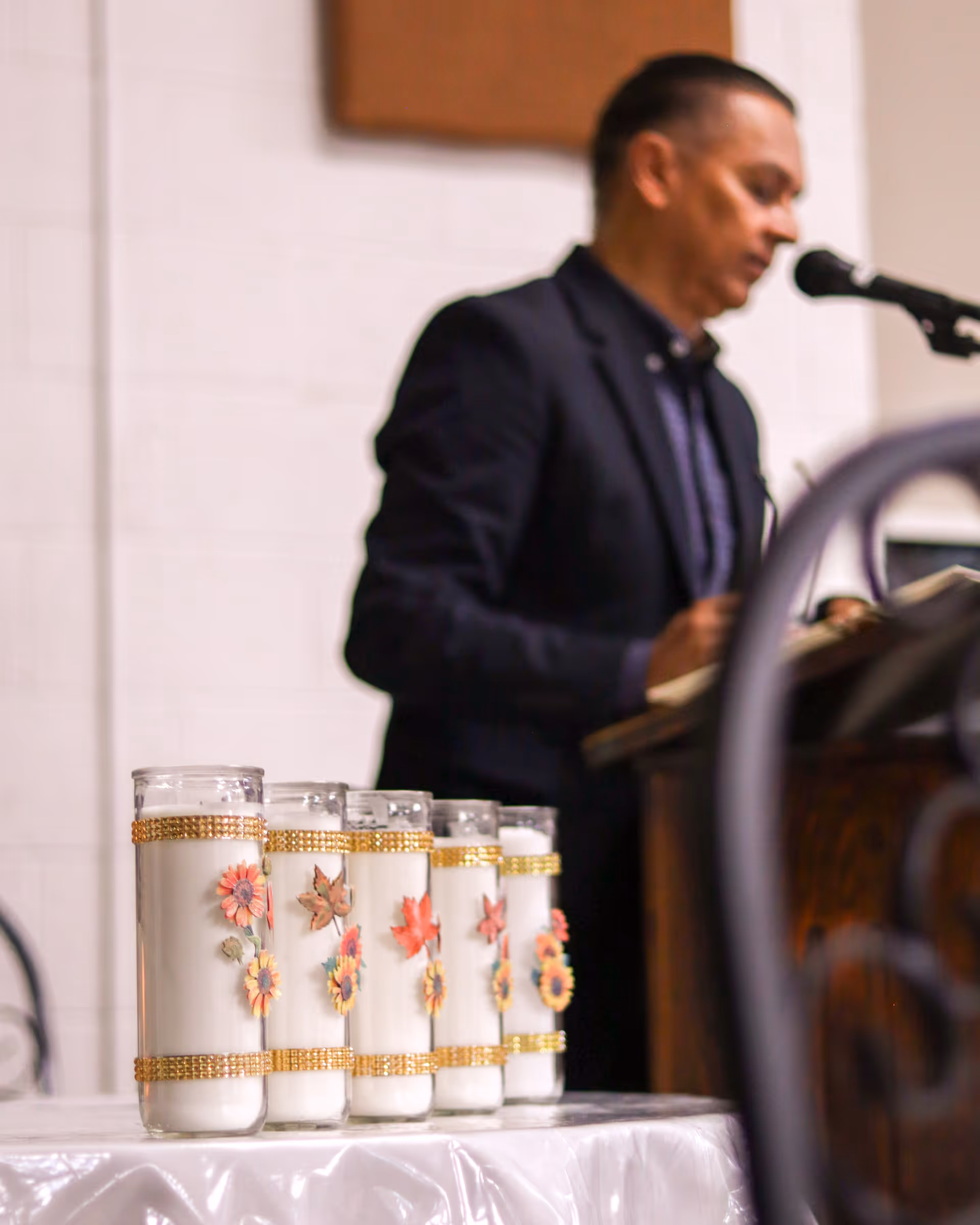 A man speaks at a podium in a dim hall beside decorative candles on a table.