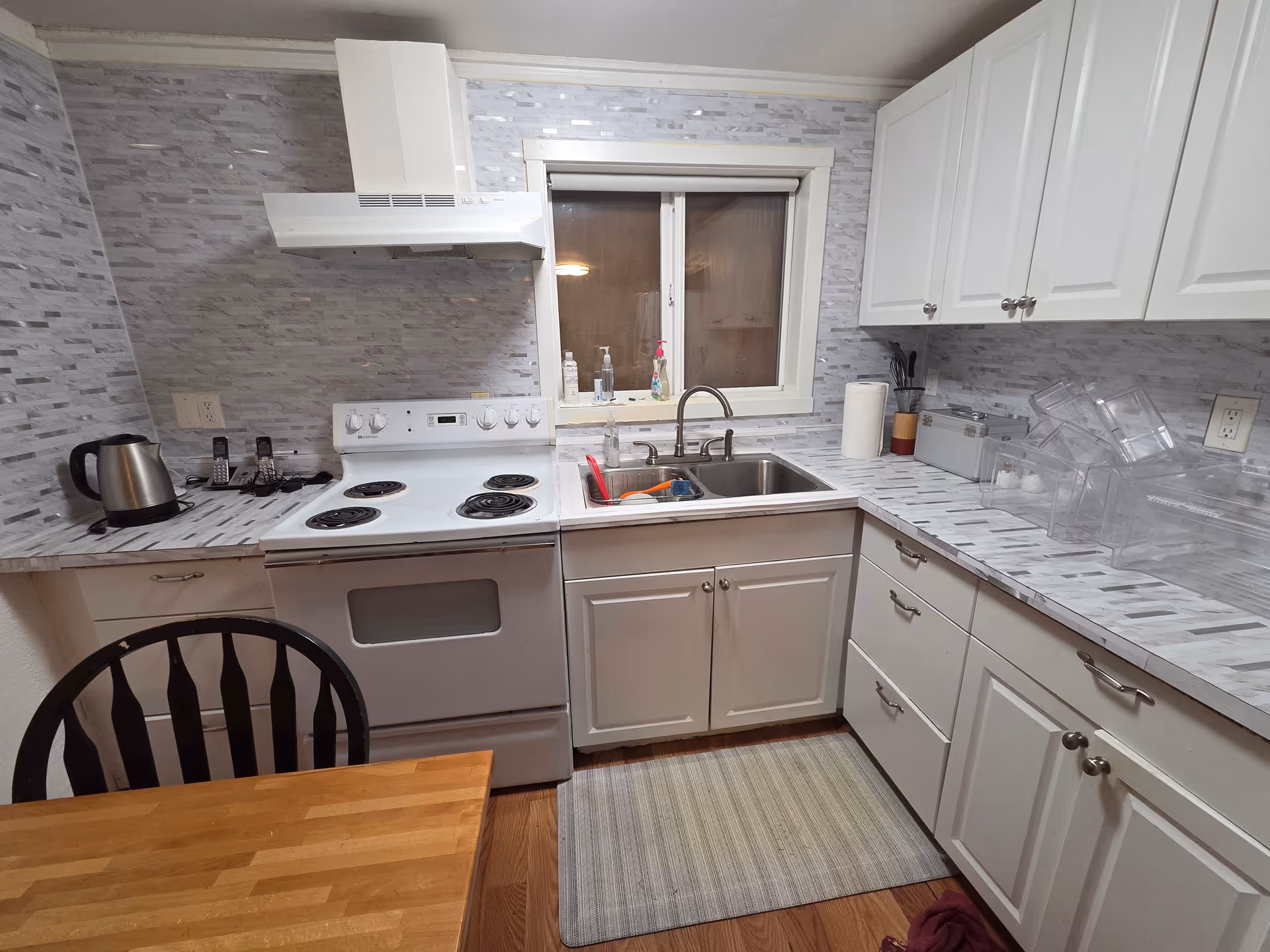Well-lit kitchen with stove, sink, white cabinets, and a wooden dining table.