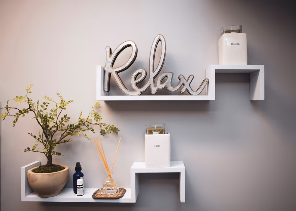 Decorative wall shelf with a metal 'Relax' sign, plant, and diffuser on a gray wall