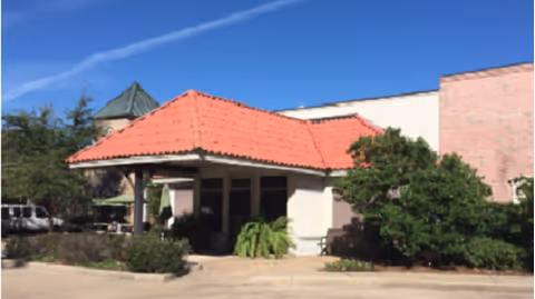 Exterior view of a senior living facility entrance with red-tiled roof and greenery.