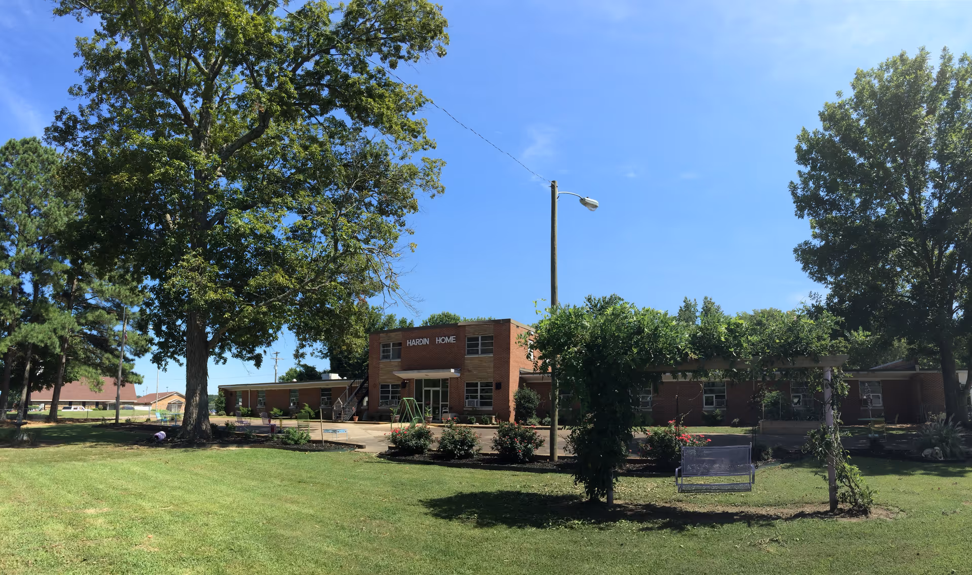 Brick senior living facility with manicured lawn and large trees against a blue sky