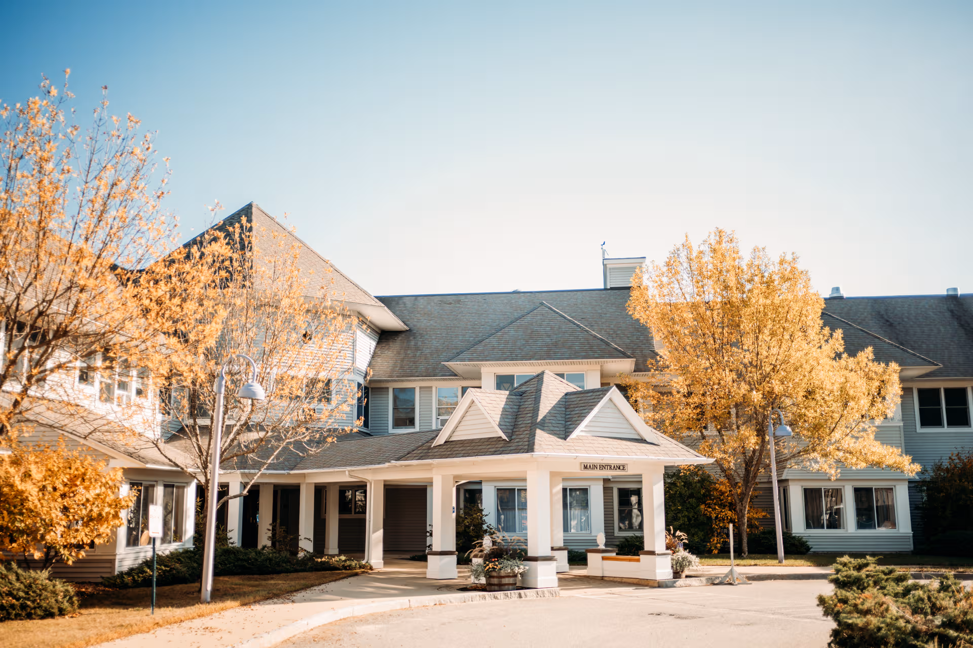 Exterior view of Birch Bay Retirement Village with a covered entrance and autumn trees.