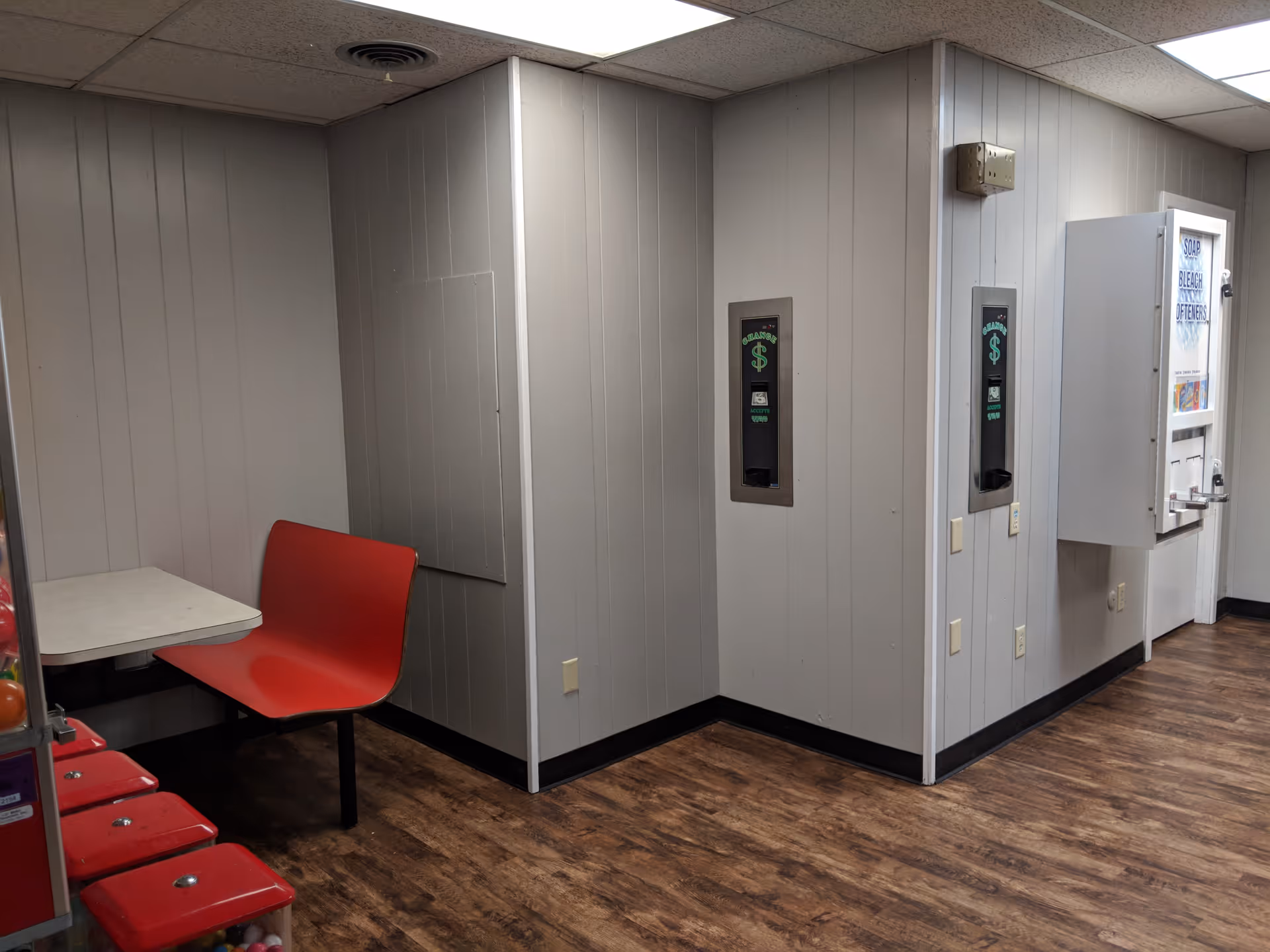 Small seating area with red chair beside a table in a gray hallway.