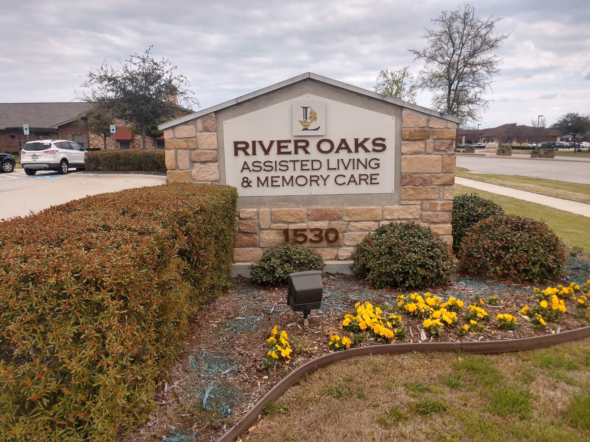 Stone sign for River Oaks Assisted Living & Memory Care with landscaping.