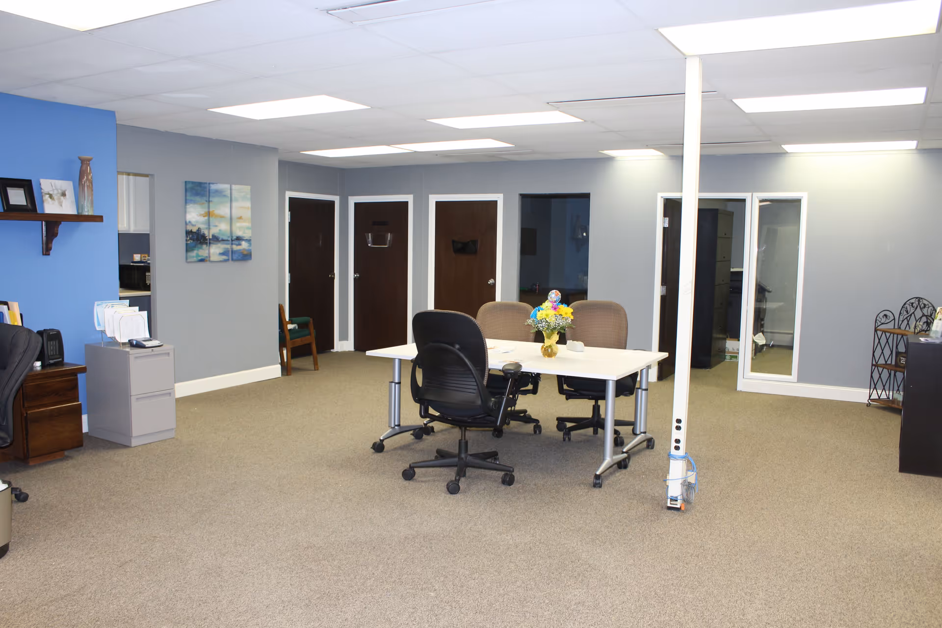 A conference-style meeting room with a central table, chairs, and a vase of flowers.