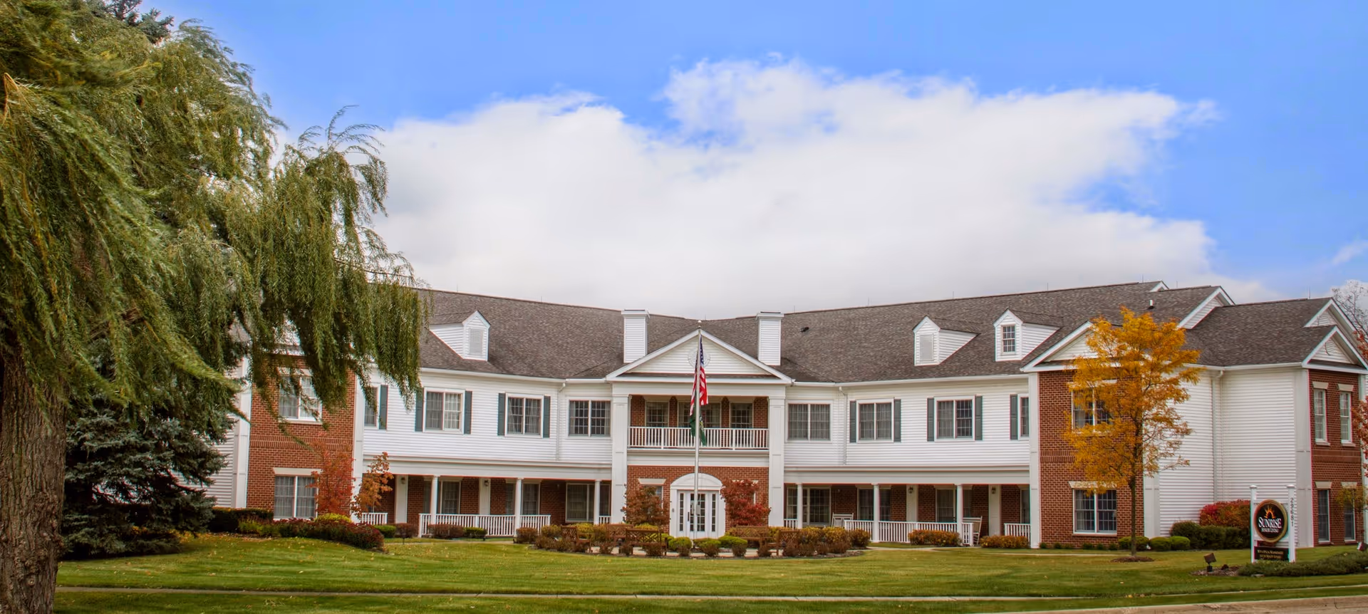 Front view of Fairmont of Farmington Hills, a large residential building with lawn and flagpole.