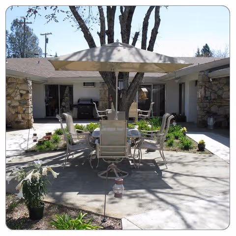 Outdoor patio at Wolf Creek Care Center with table, chairs, umbrella, and trees.