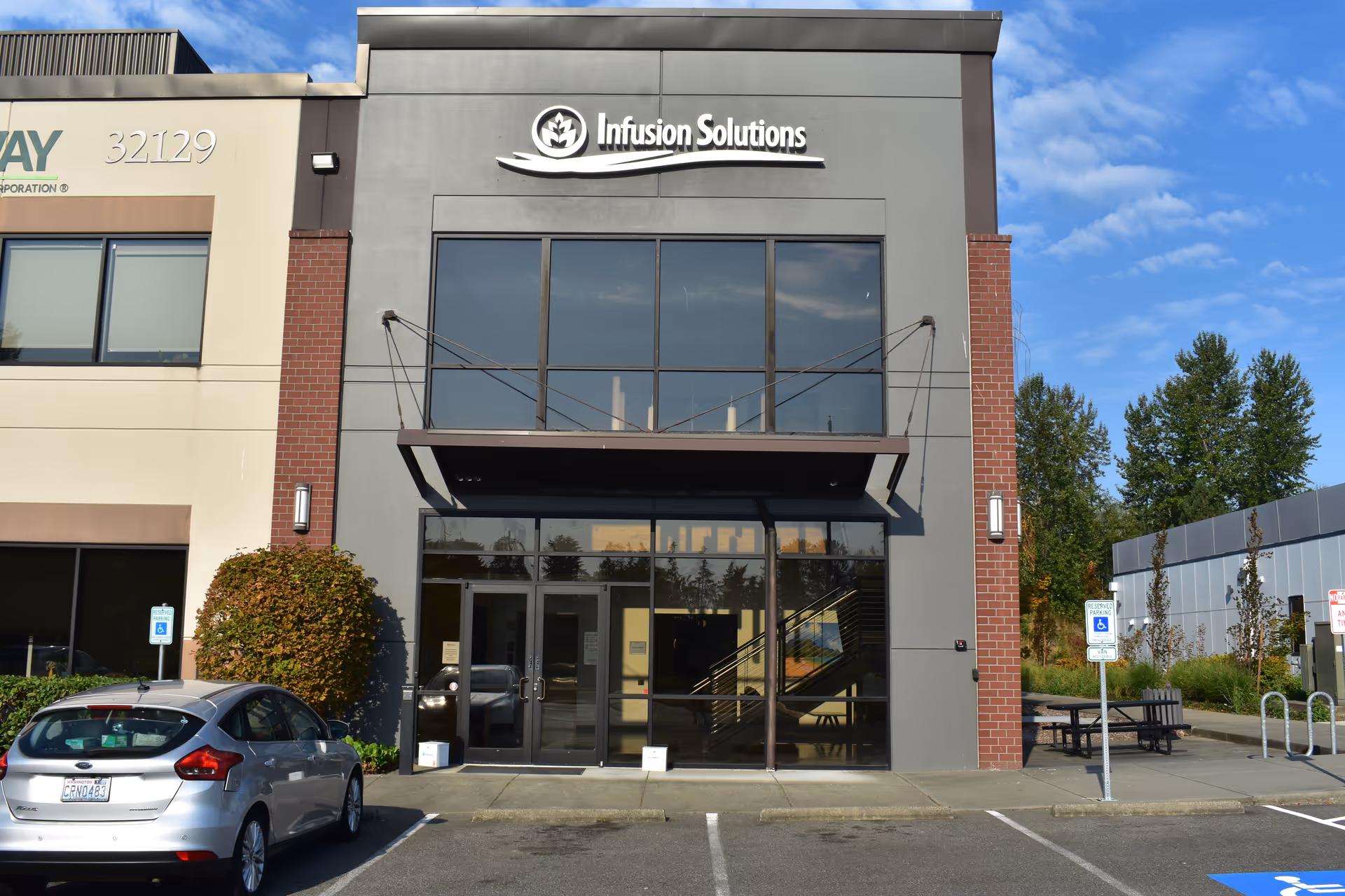 Exterior view of Infusion Solutions building with glass entrance and parked car in front.