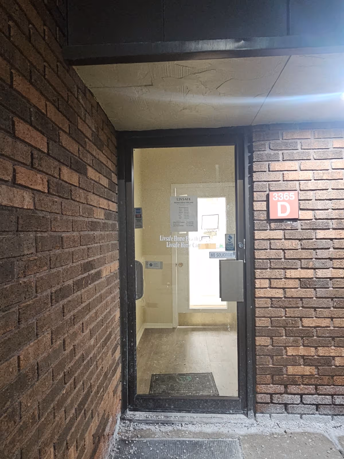 Brick building entrance with a glass door and a red unit plaque 3365 D.