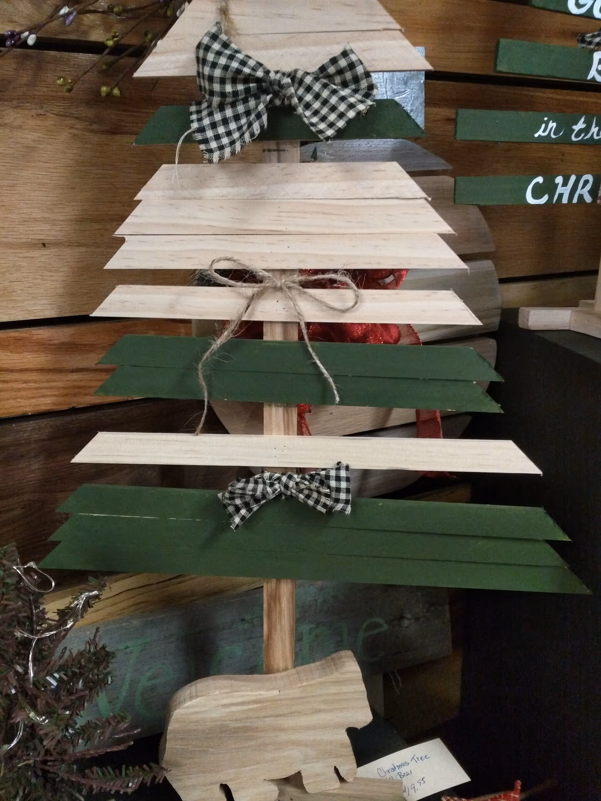 A wooden tiered Christmas tree decoration with green and white planks and checkered bows