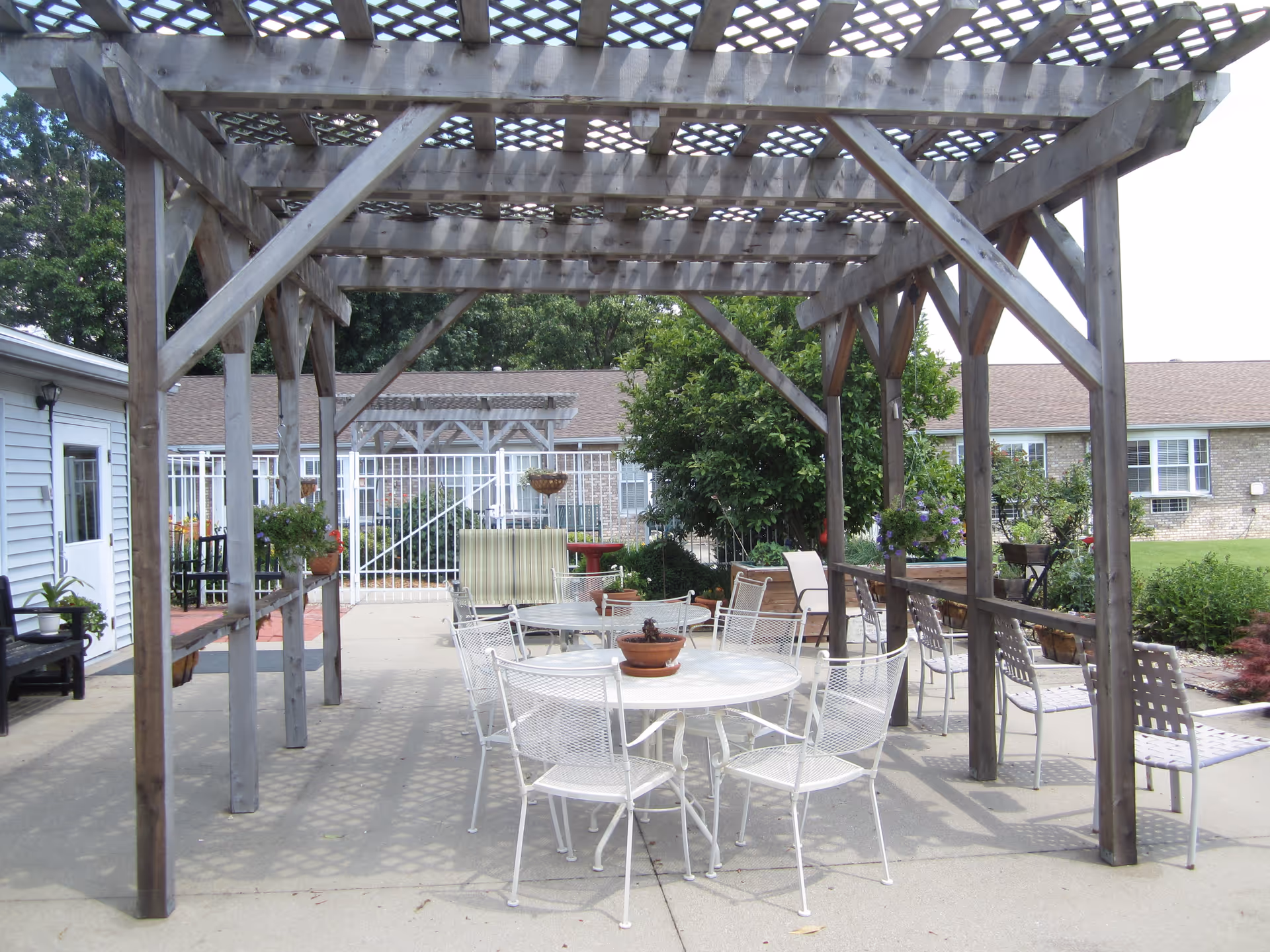 Wood pergola over a courtyard with white tables and chairs.