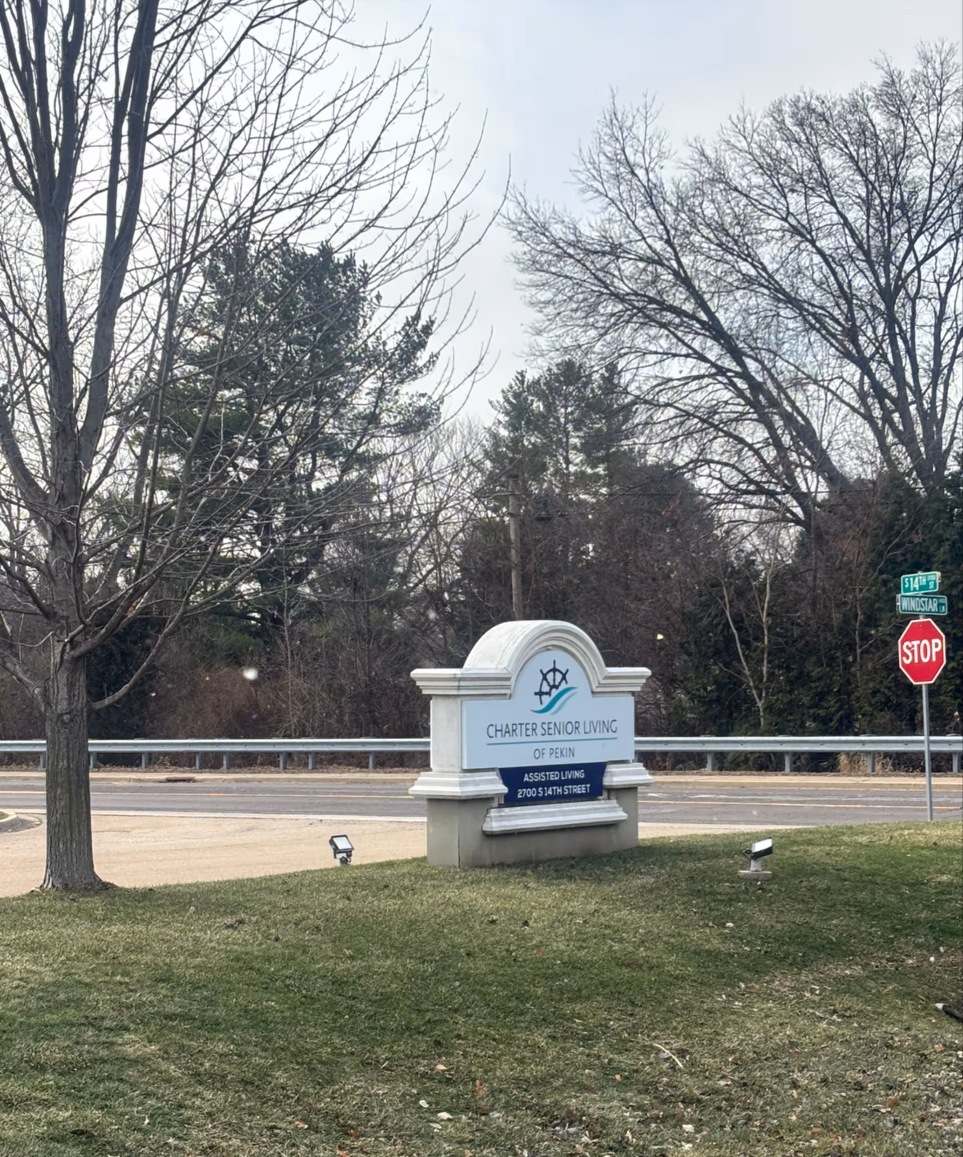 Exterior view of Charter Senior Living of Pekin sign by the road with trees nearby.