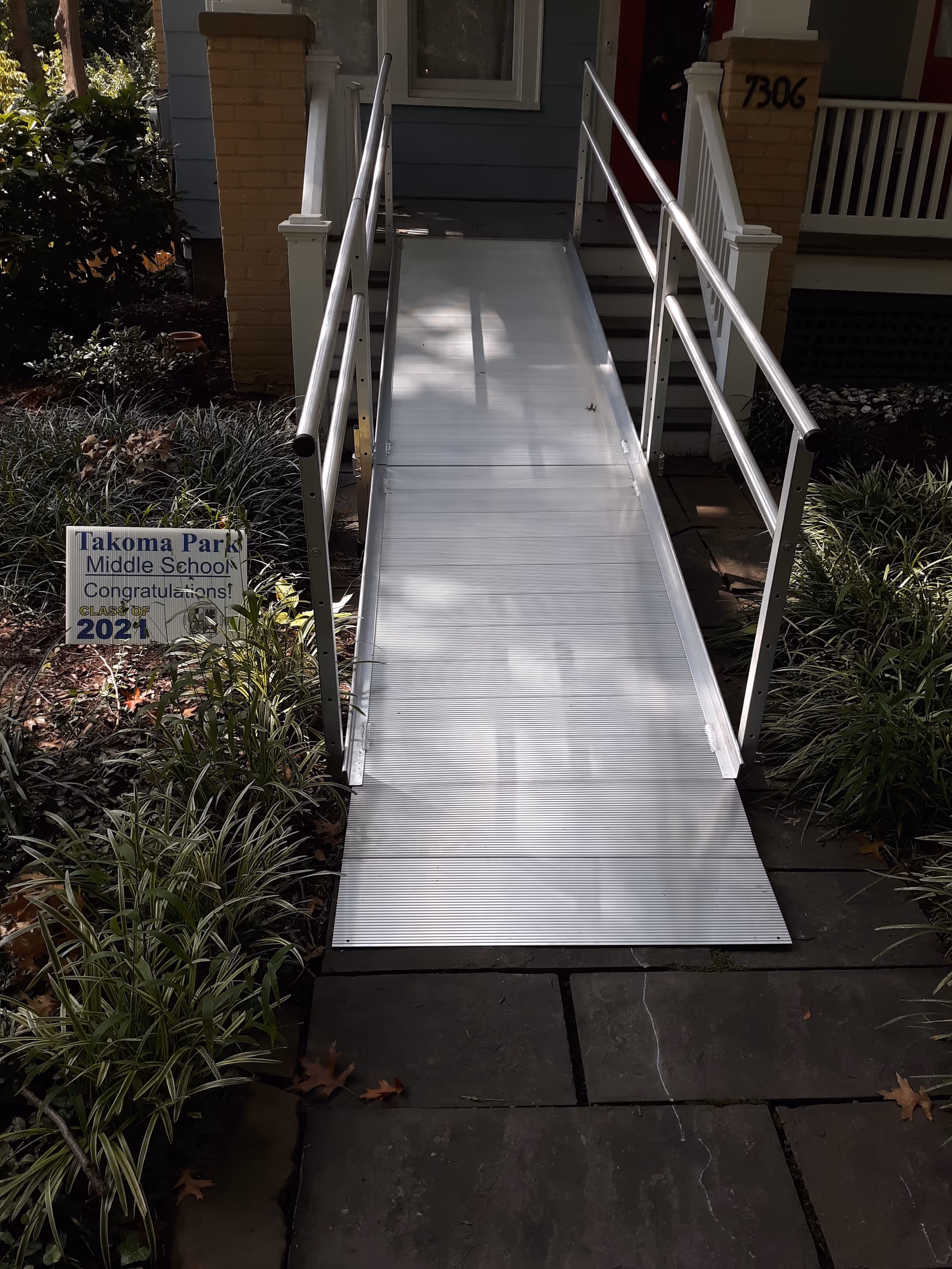 Aluminum wheelchair ramp with handrails leads to a house entrance.