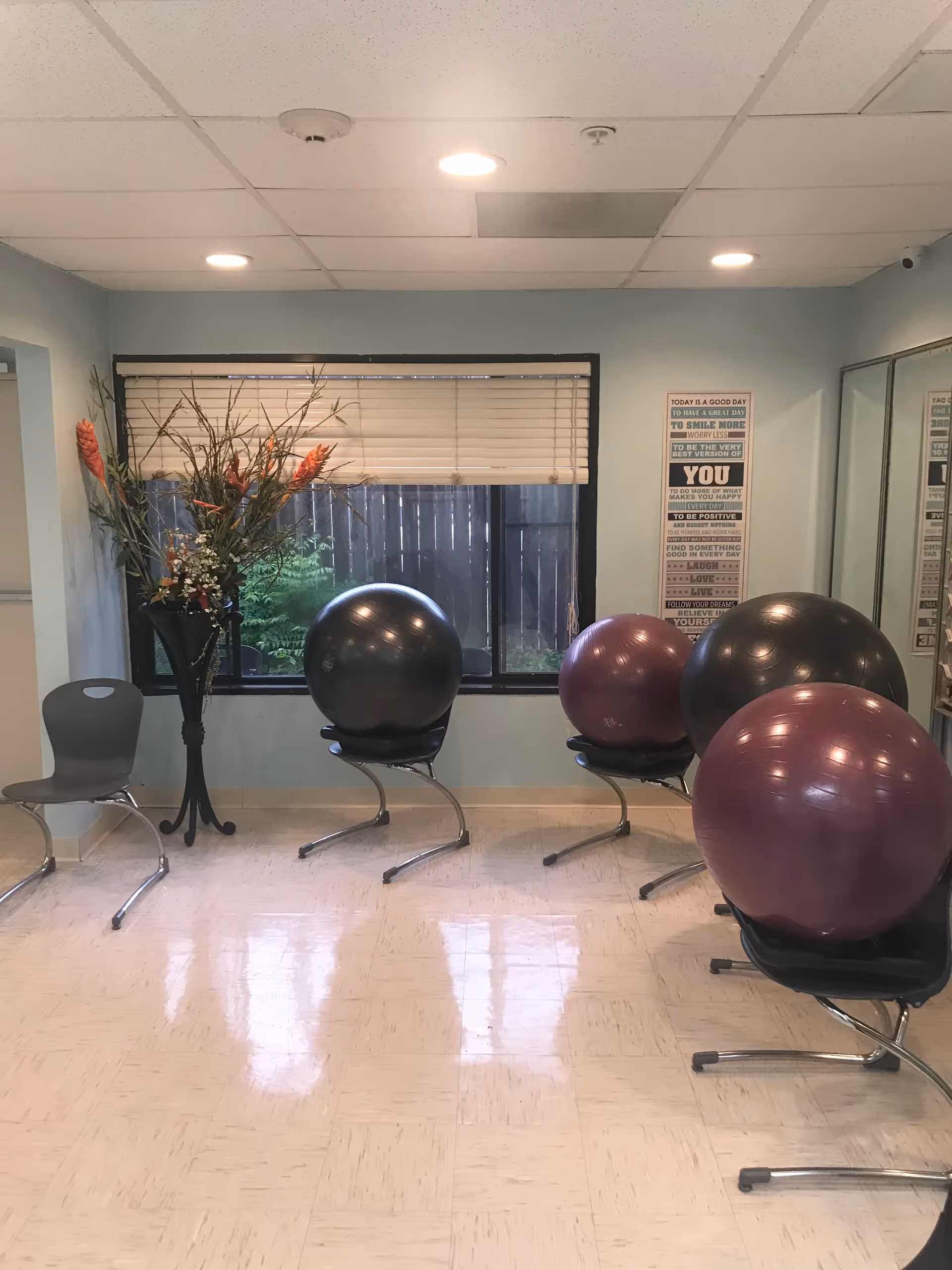 An interior room shows exercise balls on chairs near a window and a tall floral arrangement.