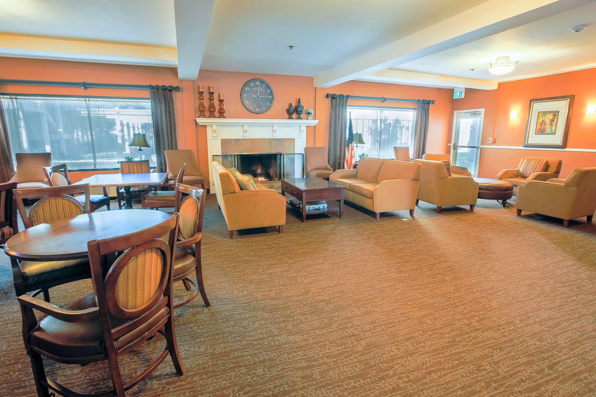 Spacious senior living lounge with sofas, chairs, a fireplace, and large windows.
