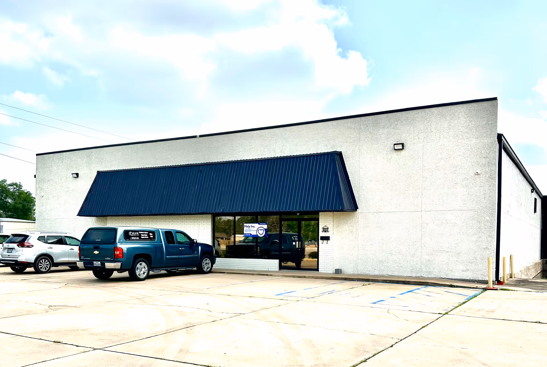 Front exterior of a building with a blue awning and parked cars.
