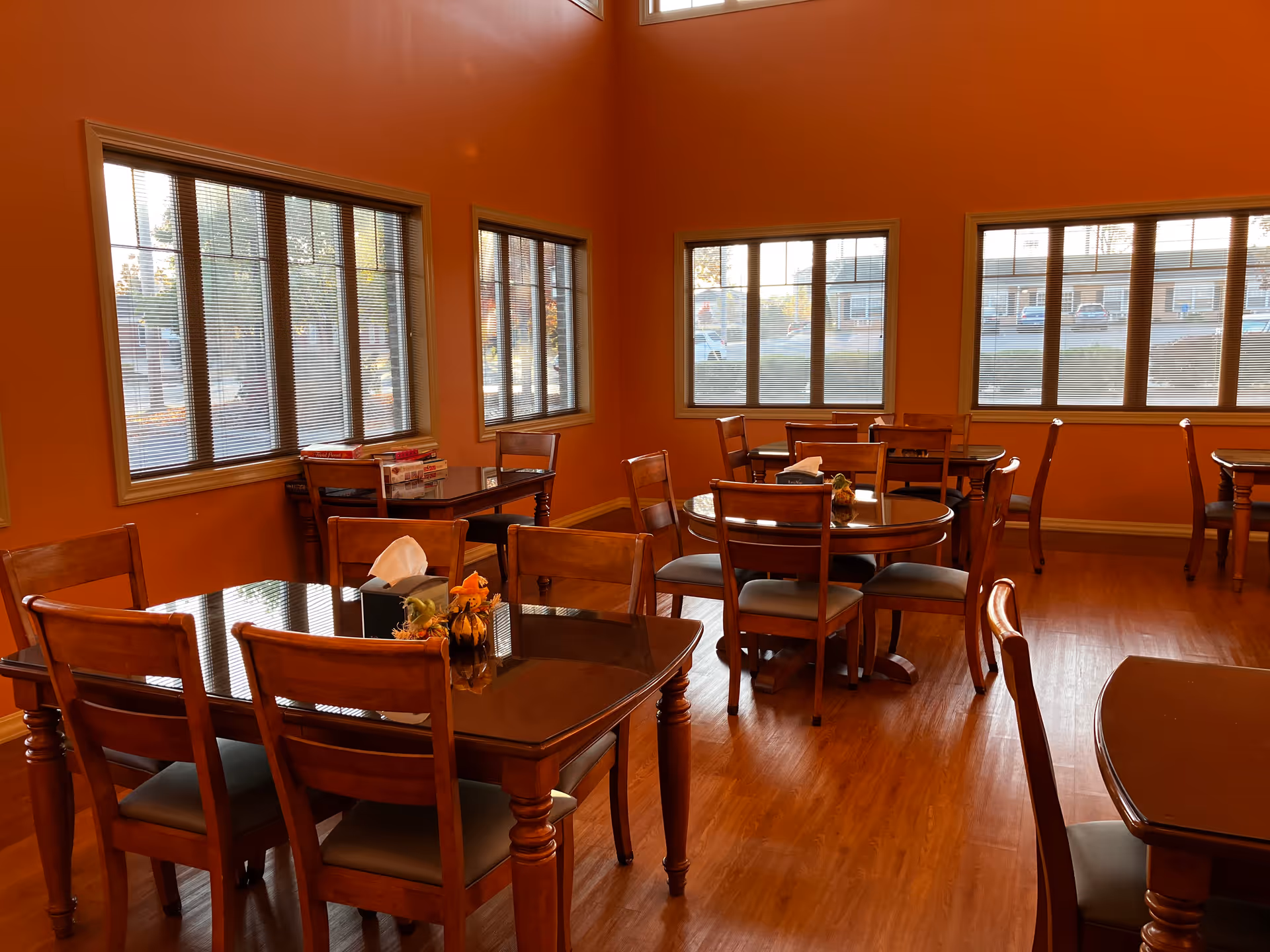 Warm orange-walled dining room with wooden tables, chairs, and large windows.