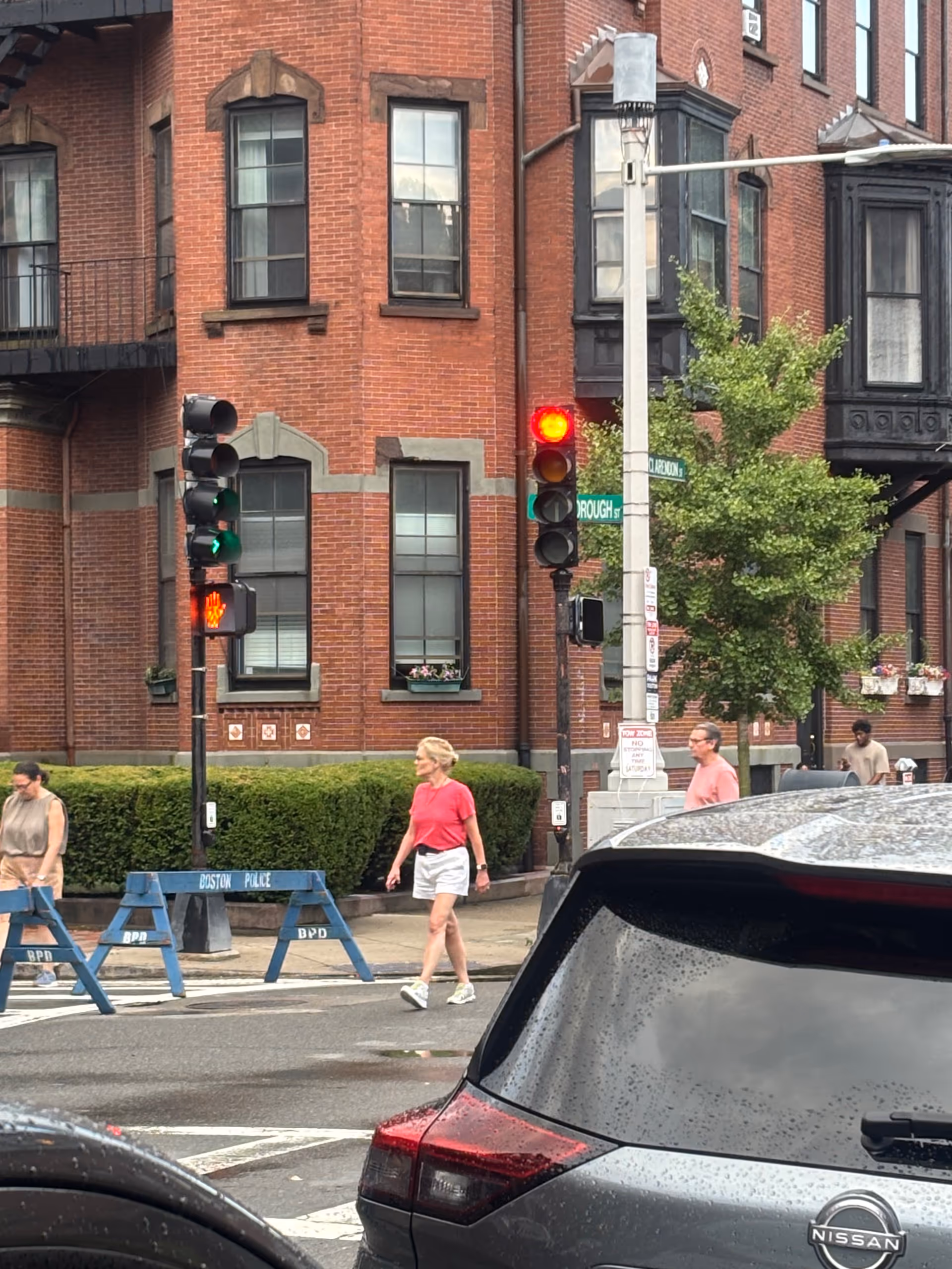 Urban street scene with pedestrians, brick building, traffic lights, and a parked car.