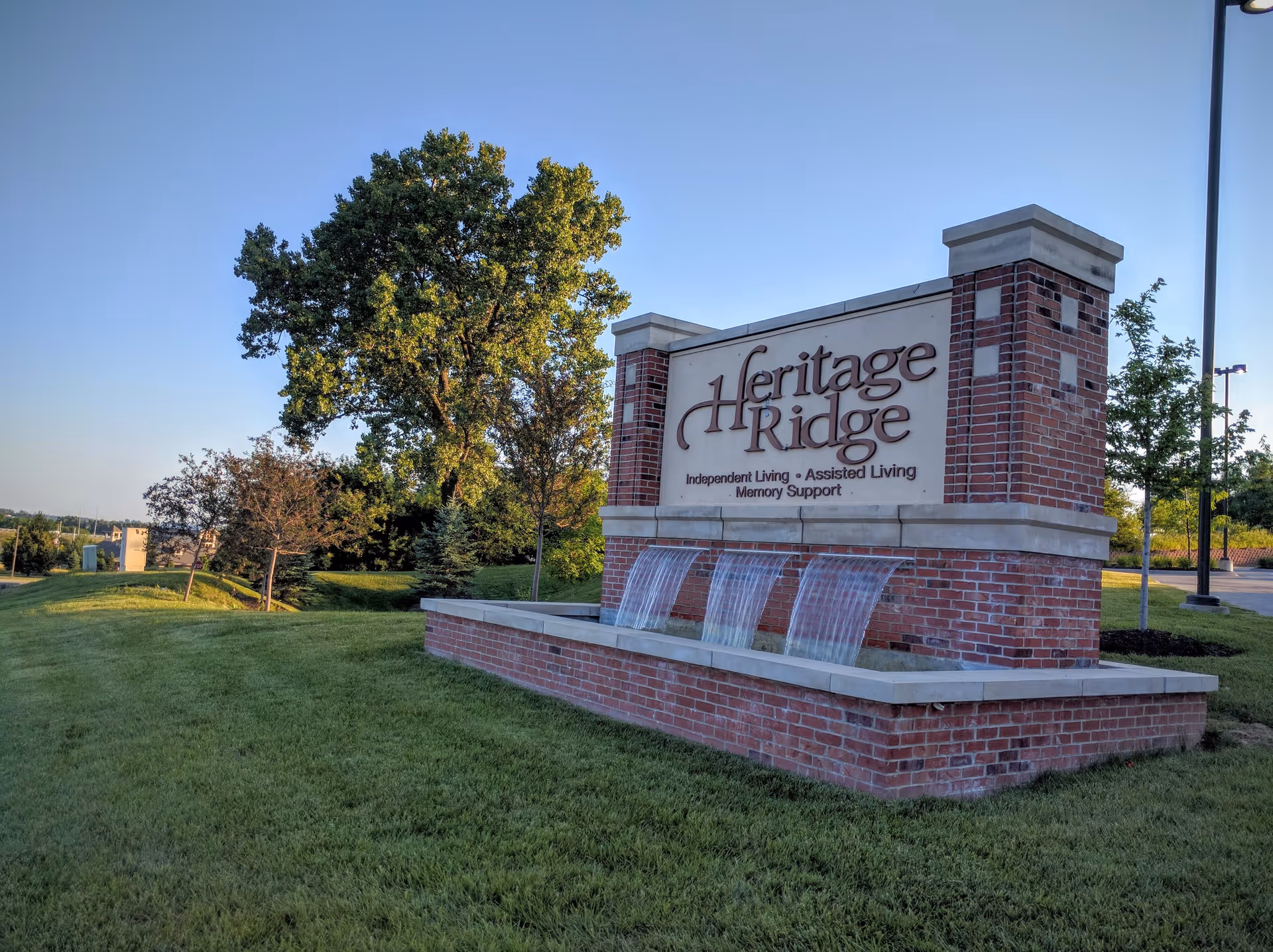 Heritage Ridge Retirement Community brick sign with cascading water features on green lawn.